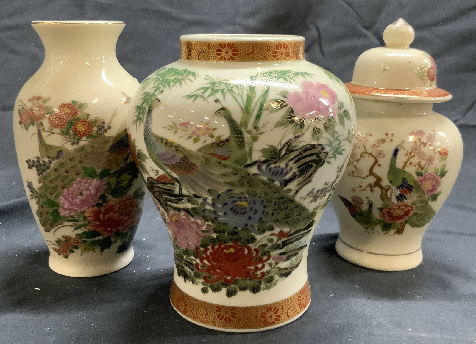 Signed Lot 3 Asian Porcelain Vases & Urn W Lid: Undersides of each piece are signed with chop signatures. Lot includes 2 vases & 1 urn with lid. Each piece is cream with intricate multi toned floral, leaf & peacock detail. Largest vase measures app