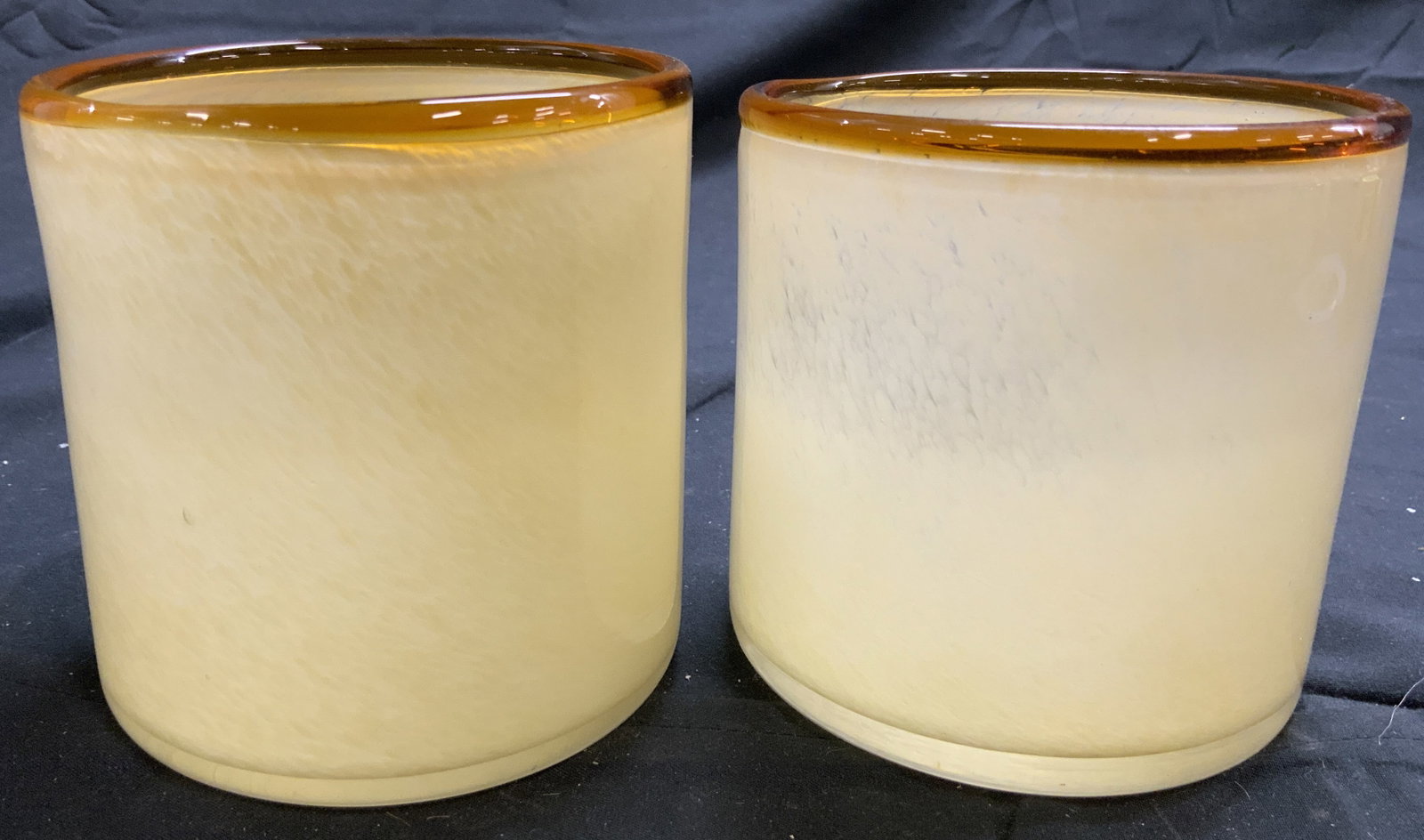 SEVILLE Pr Art Glass Candle Holders Vessels: Undersides are marked SEVILLE. Lot includes 2 candle holders. Each are cream with amber toned rims. Each vessel is glass. Candle holders each have cylindrical forms. Each measures approximately 4 inch
