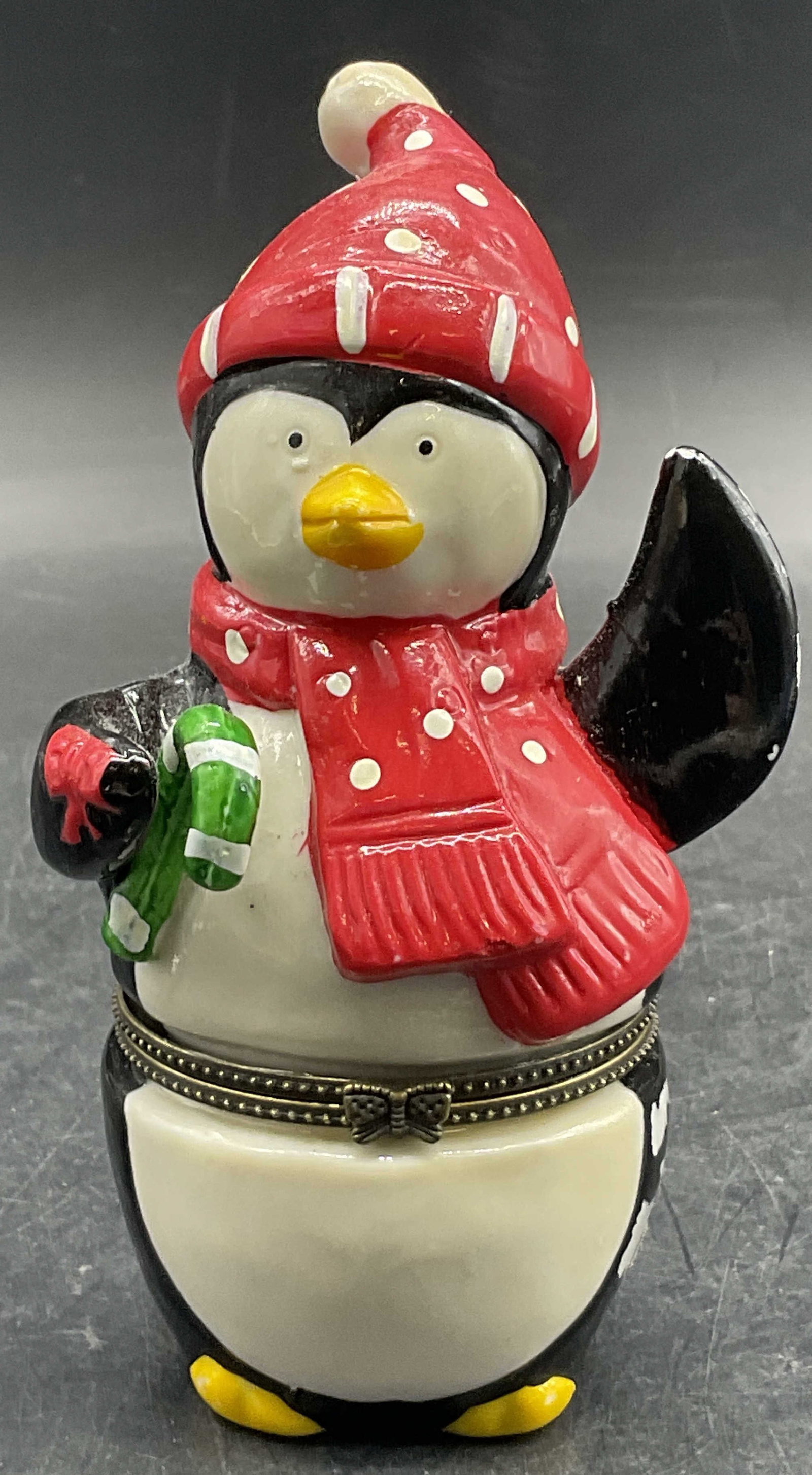 Ceramic Winter Fashion Penguin Hinged Trinket Box: Ceramic Winter Fashion Penguin Hinged Trinket Box. Penguin wears a hat and scarf. Opens with metal hinge hardware. Measures approx. 5H x 2.25W in. Losses to finish, residue, and surface wear present. 