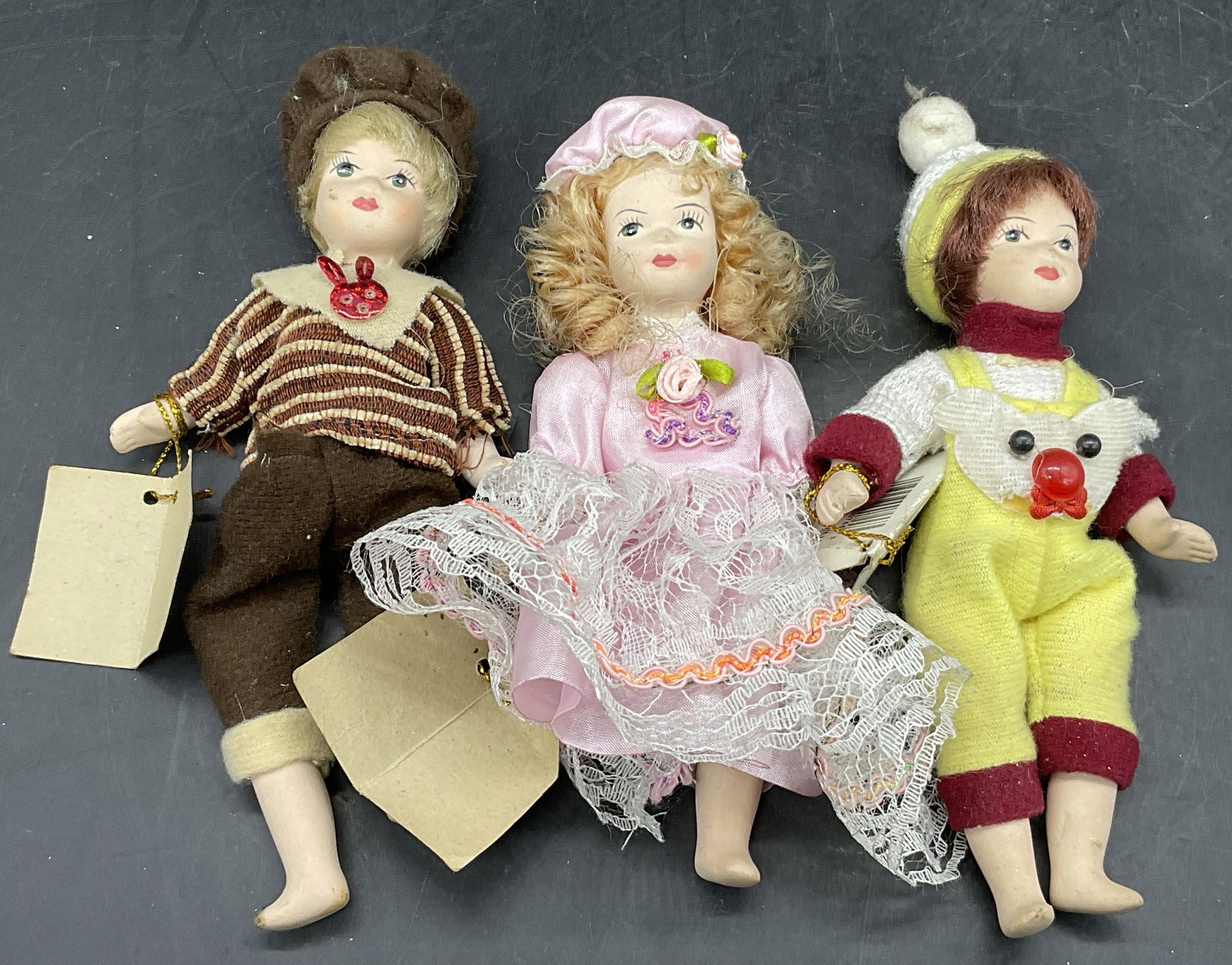 Lot 3 DEPENDABLE IND INC Porcelain Dolls, Org Tags: Porcelain Dolls With Fabric Clothing. Original tags attached. Tags read Distributed by DEPENDABLE IND INC. Pieces are similar is size measuring approx. 7L x 2.5W in. Some missing limbs, discoloration,