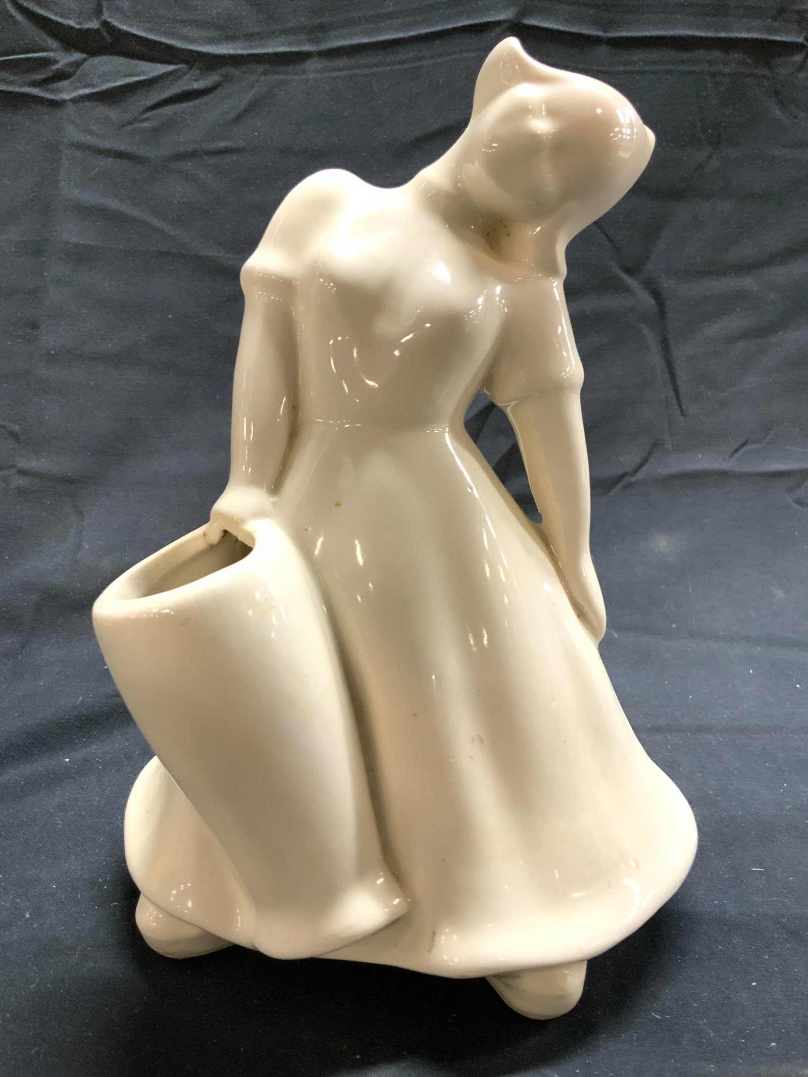 Vintage Porcelain Dutch Girl Vase: Vase is cream toned and porcelain. Piece depicts a Dutch girl figure wearing a hat leaning to one side holding a vase in one hand. Vessel appears to be vintage. Piece measures approximately 8 inches t