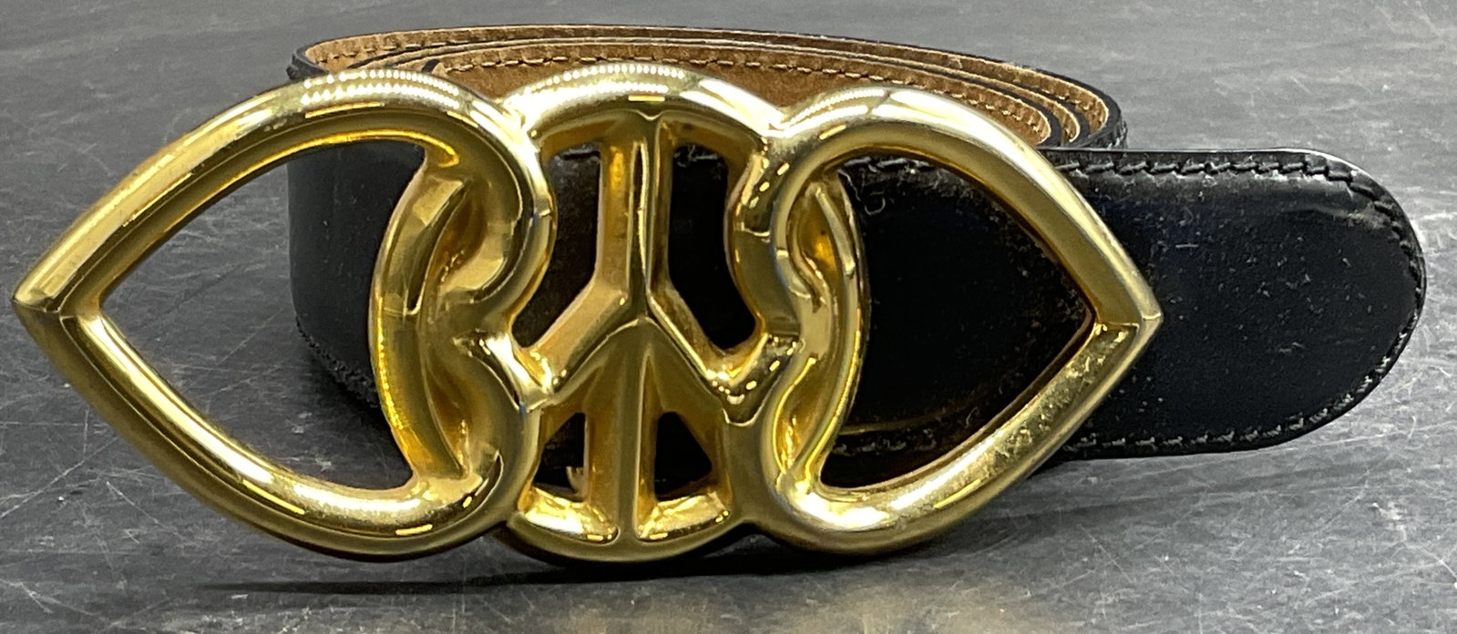 Double Heart Peace Sign Belt Buckle W/ Belt: Double Heart Peace Sign Belt Buckle Attached to Black & Brown Leather Belt. Belt buckle is crafted from gold tone metal. Belt appears to be leather, possibly leather style. Total length of pieces meas