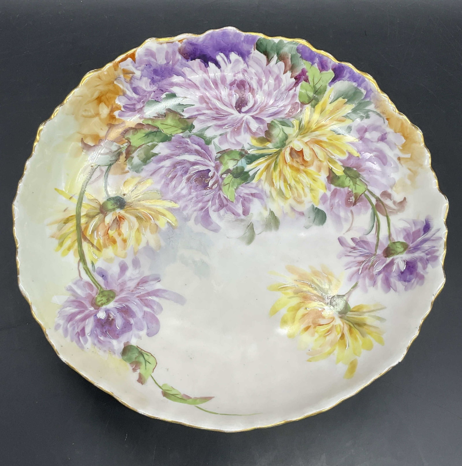 HOHENZOLLERN GERMANY Floral Porcelain Footed Dish: Vintage hand painted floral motif porcelain footed dish. Scalloped rim. Multicolored hues with gilt line work. Primarily yellow, purple, and green hues. Measures approx. 2.5H x 10.5W in. Underside sig