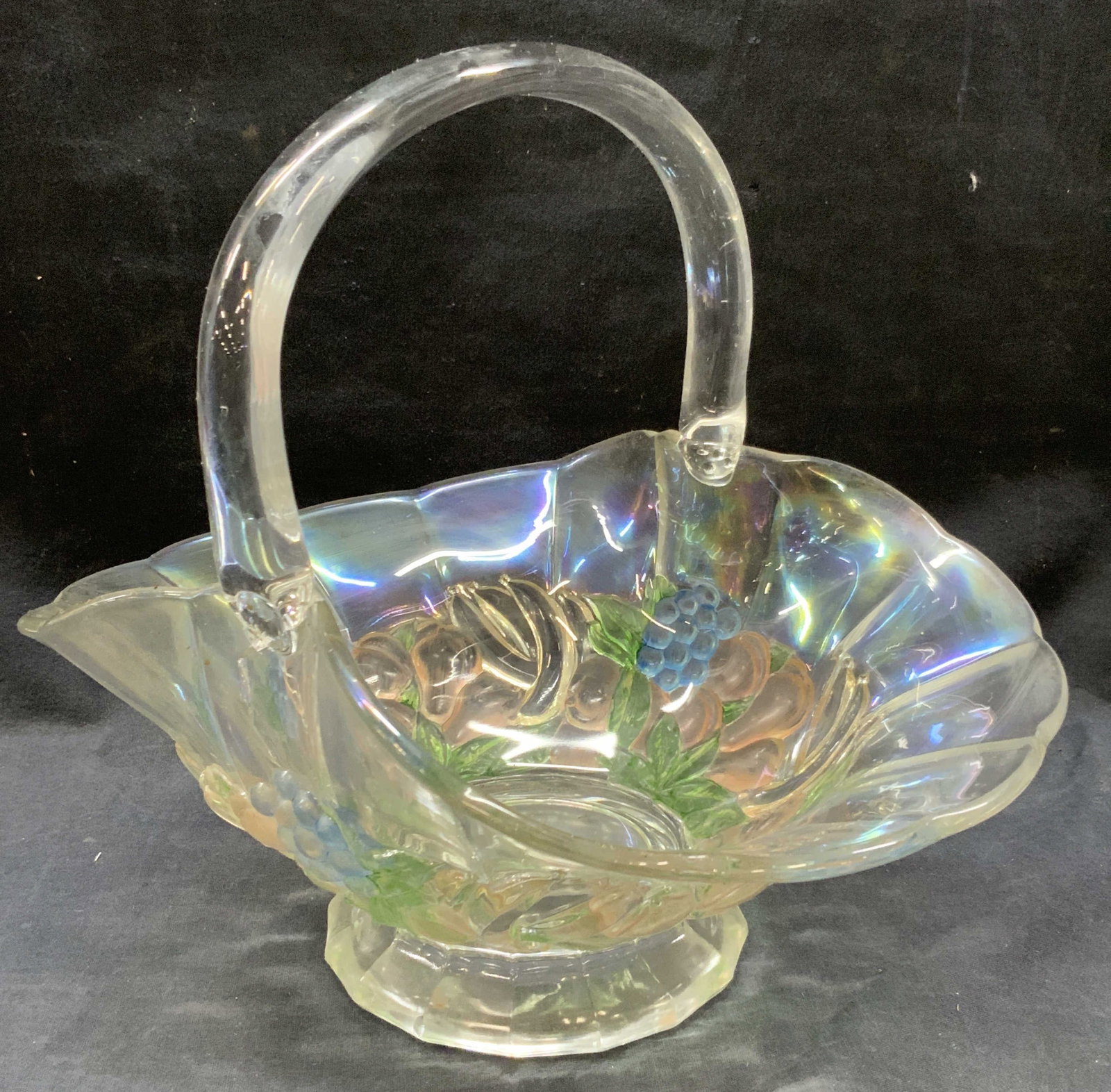 Vintage Art Glass Basket: Vintage Iridescent clear glass basket with top handle and raised motifs of fruit and floral sun blue and pink on exterior of basket. Approx 11 inches tall and 8 inches wide and evident cracking to sid