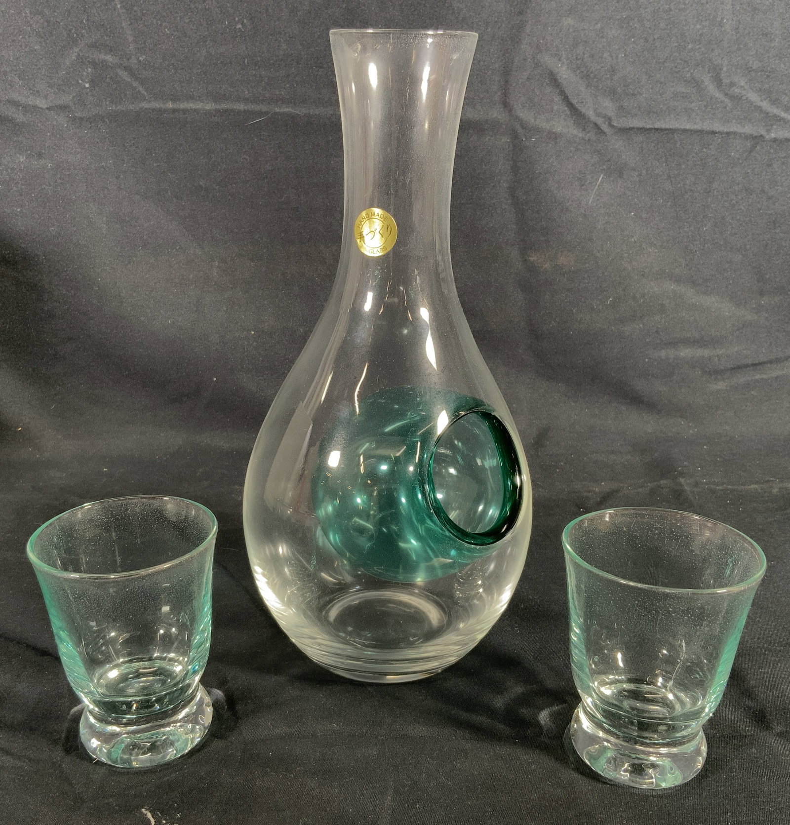 Utsuwa-No-Yakata Asian Glass Sake Decanter: Handmade glass decanter and two shot glasses. Utsuwa-No-Yakata brand. Glass decanter has a blue hollow bulb on side. Two shot glasses have footed base. Decanter measures approx. 8.5 H x 4 D in. Shot g