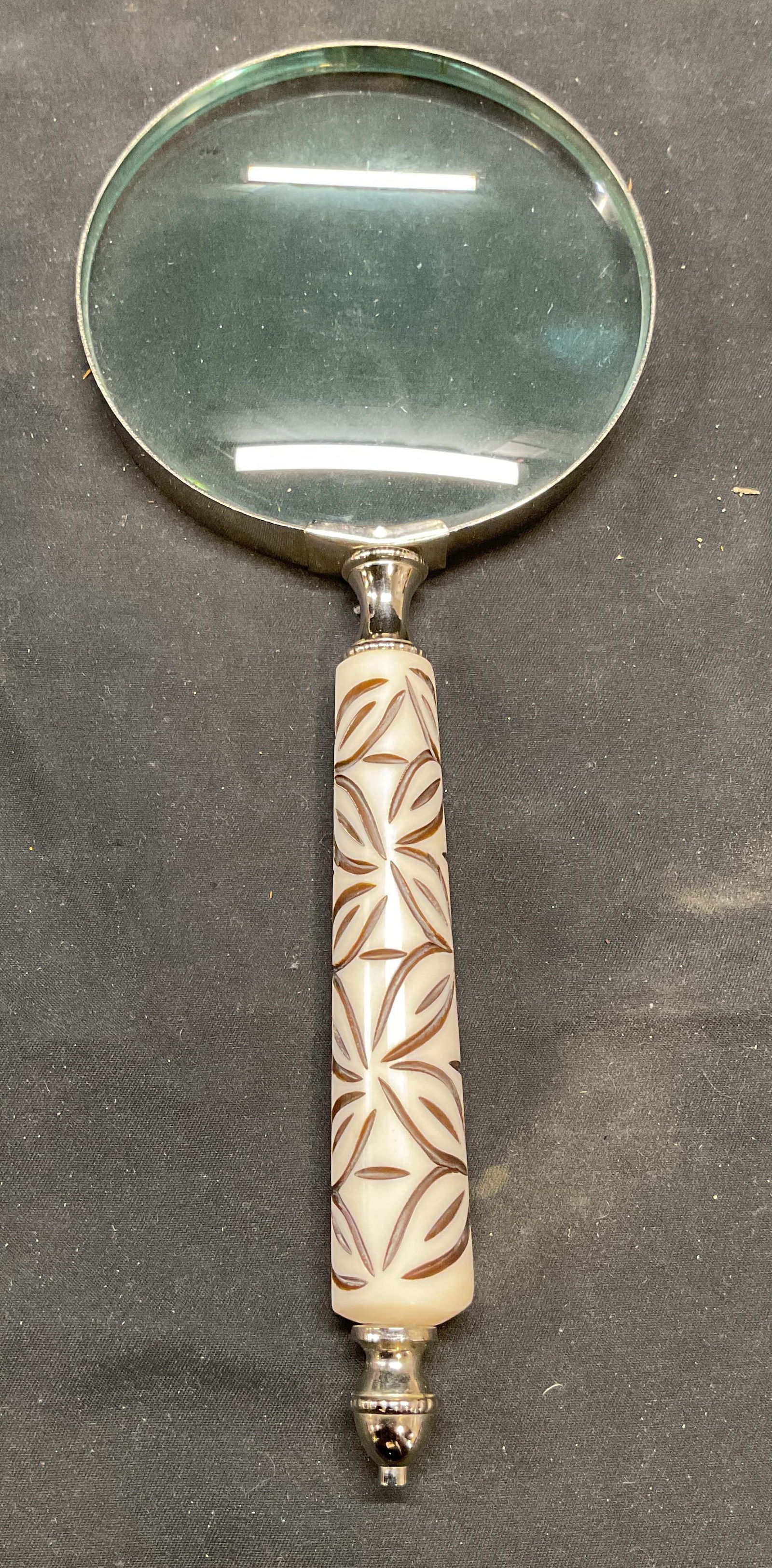 Carved White Handle Magnifying Glass: Magnifying glass with carved white handle. Silver tone metal, glass, composite material. Measures approx. 9.5 inches long. Some surface wear consistent with exposure. Magnifying glass, white magnifyin