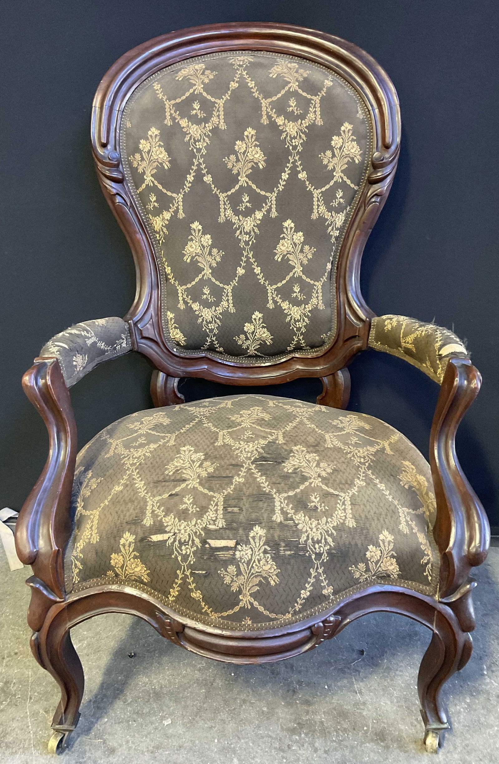 Antique Upholstered Parlor Chair On Casters: Antique, possibly vintage, upholstered parlor chair on casters. Carved wood frame. Measures approx. 41H x 25W x 23D in. Discoloration, surface wear, losses, tears, and separation present. Casters need