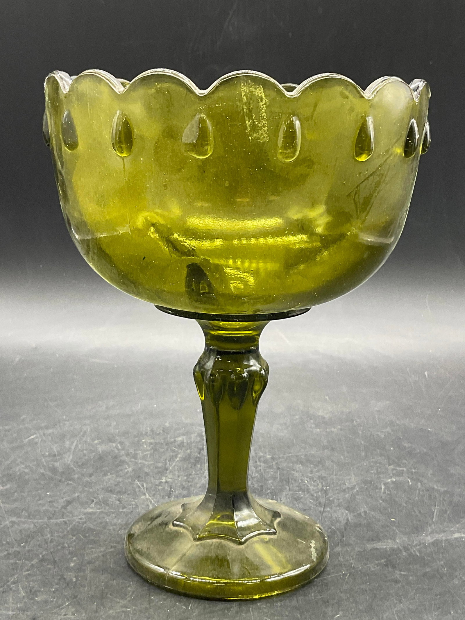 Vintage Green Glass Pedestal Compote Bowl: Vintage Green Glass Pedestal Compote Bowl. Scalloped edge. Measures approx. 7.5H x 5.5W in. Bubbles to glass. Seam present. Surface wear, residue, and chipping present. home decor, home accents, homew