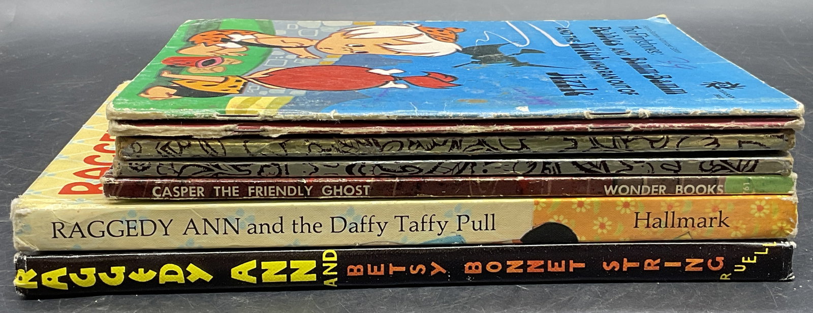 Lot 7 Vintage Childrens Books, The Flintstones +: Group Lot Seven Vintage Childrens Books. Includes books that feature Raggedy Ann, The Flintstones, Tom & Jerry, and more. Losses, discoloration, loose pieces, writing, and surface wear present. Book t