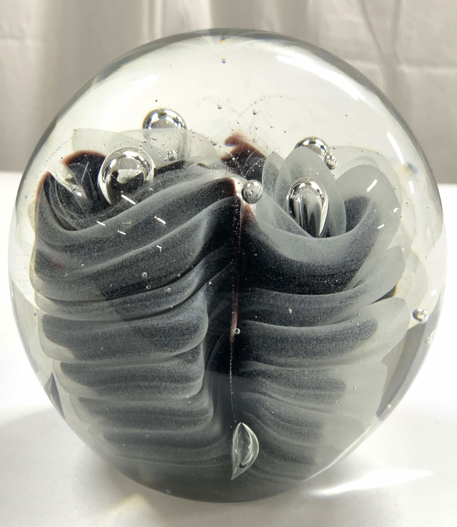 Handblown Art Glass Paperweight: Paperweight is glass. Piece appear to be hand blown. Paperweight has slate and black toned inner detail in addition to bubble detail. Piece has spherical form. Paperweight measures approximately 4 inc