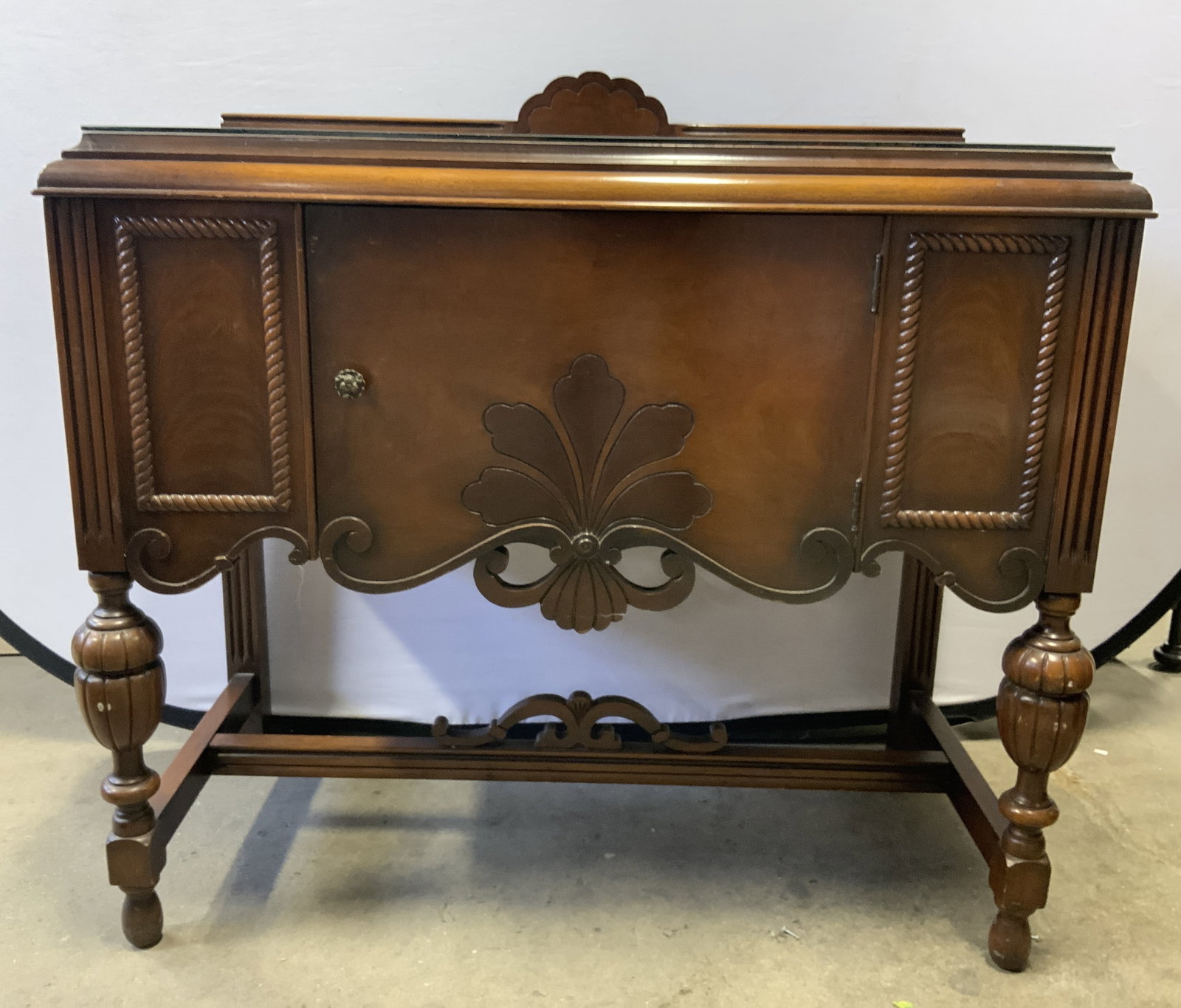 Vntg Jacobean Sideboard Server W Glass Top: Sideboard server is brown toned and wooden. Piece includes glass top. Sideboard is vintage piece has 1 cabinet door, 4 carved wooden legs with stretchers in between. Sideboard server is Jacobean style