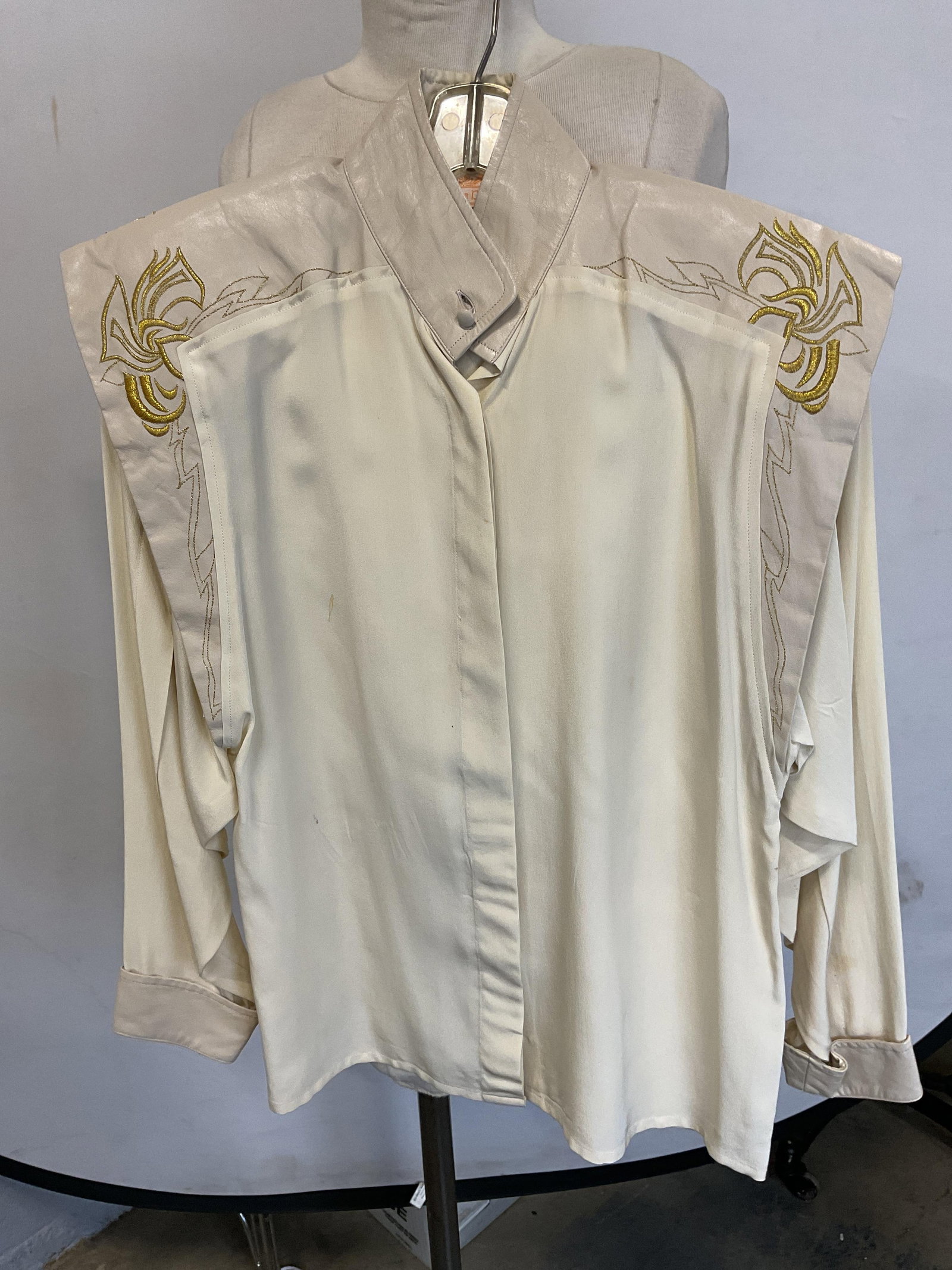 Mary Jane Denzer White Faux Leather Top: Mary Jane Denzer white satin and faux leather trim long sleeve button up top. Metallic gold embroidered detail. Measures approx 17 inches across chest. Some blemishes observed. Mary Jane Denzer, desig