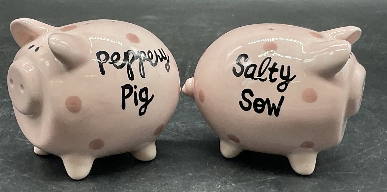 LORRIE VEASEY Salty Sow & Peppery Pig Shakers: Pig shaped ceramic salt and pepper shakers. Salty Sow and Peppery Pig set by Lorrie Veasey. Underside signed Lorrie Veasey, OUR NAME IS MUD. Measures approx. 2.5H x 3W in. Sticker residue and surface 