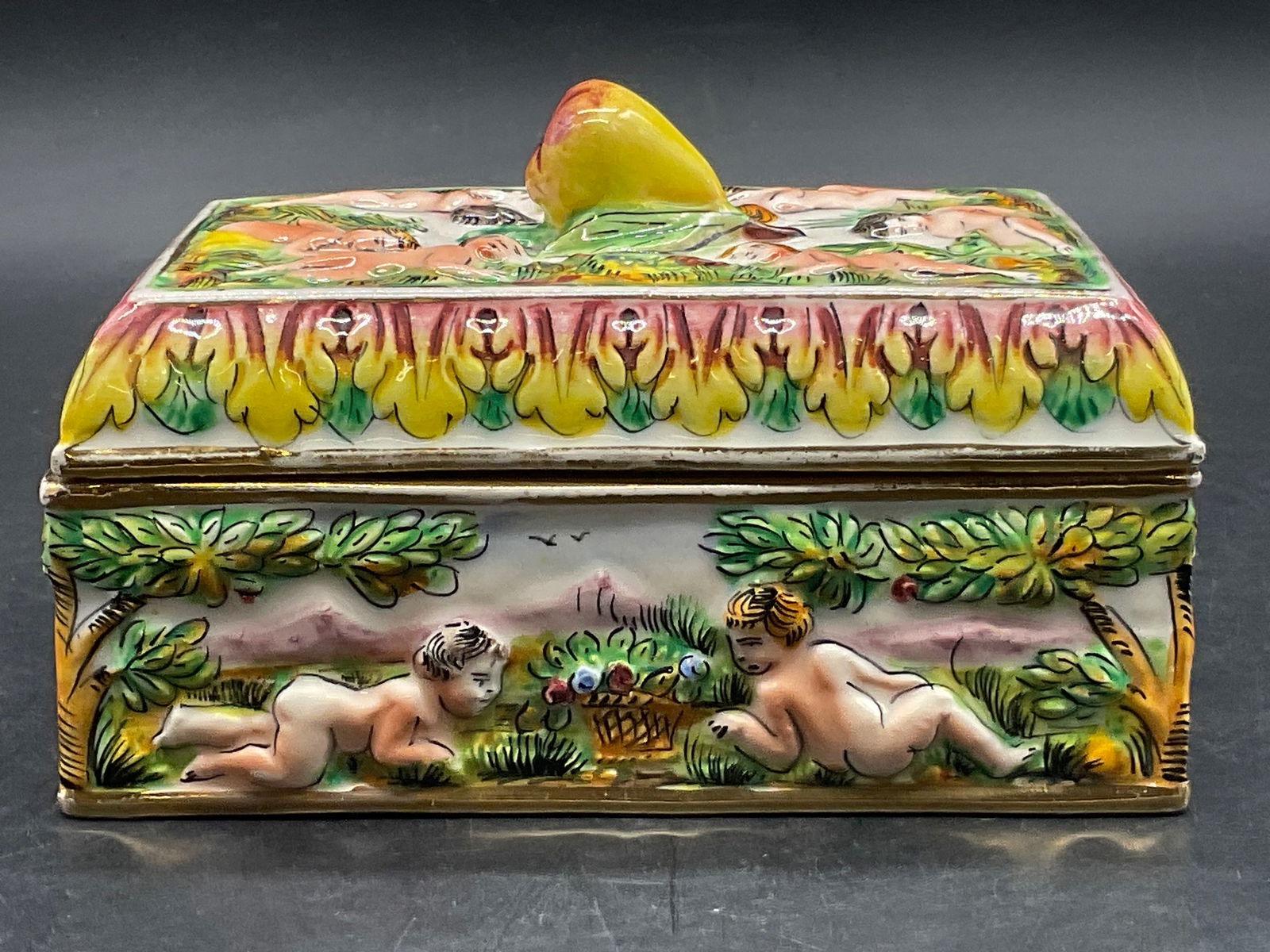 Vntg CAPODIMONTE Italian Ceramic Trinket Box, Lid: Vintage CAPODIMONTE Hand Painted Italian Ceramic Trinket Box. Lidded. Underside is trademarked and reads ITALY. Nude figures throughout. Measures approx. 4H x 6W in. Surface wear, pitting, chipping, a