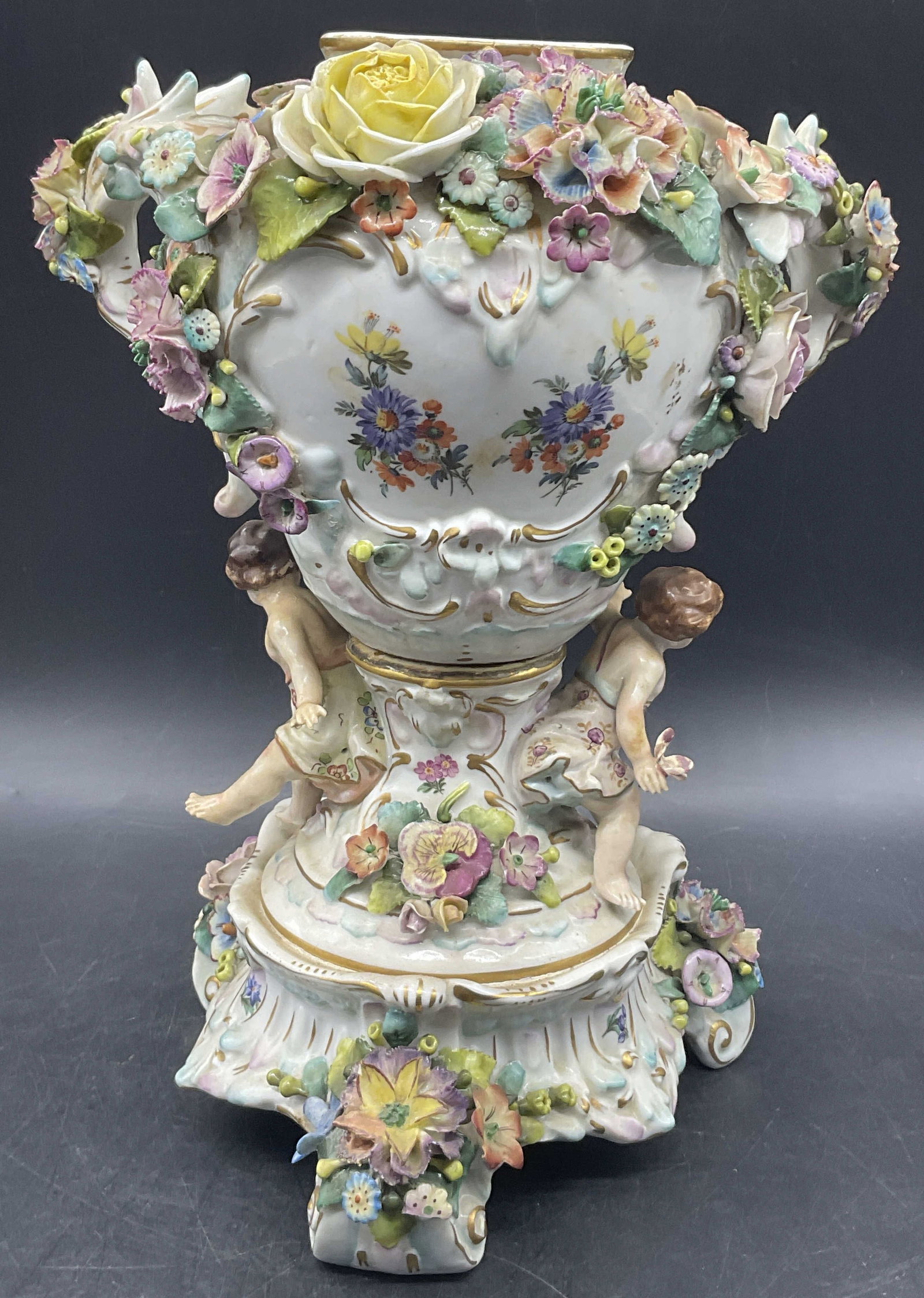 Vntg Trademarked Floral & Figural Porcelain Vase: Vintage Trademarked Floral & Figural Motif Porcelain Vase. Raised florals, foliage, and figures to the piece. Measures approx. 11.5H x 9.5W in. Trademarked to the underside, possibly Dresden. Weighty.
