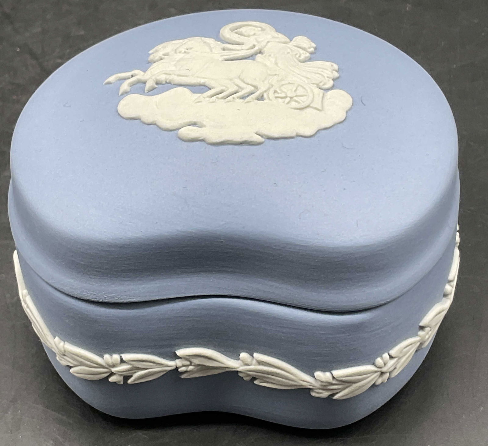 WEDGWOOD BLUE JASPERWARE Trinket Box, England: WEDGWOOD BLUE JASPERWARE Pottery Trinket Box. Lidded. White hued raised laurel to the sides and a chariot motif to the lid. Underside signed WEDGWOOD ENGLAND. Measures approx. 2H x 3W in. Surface wear