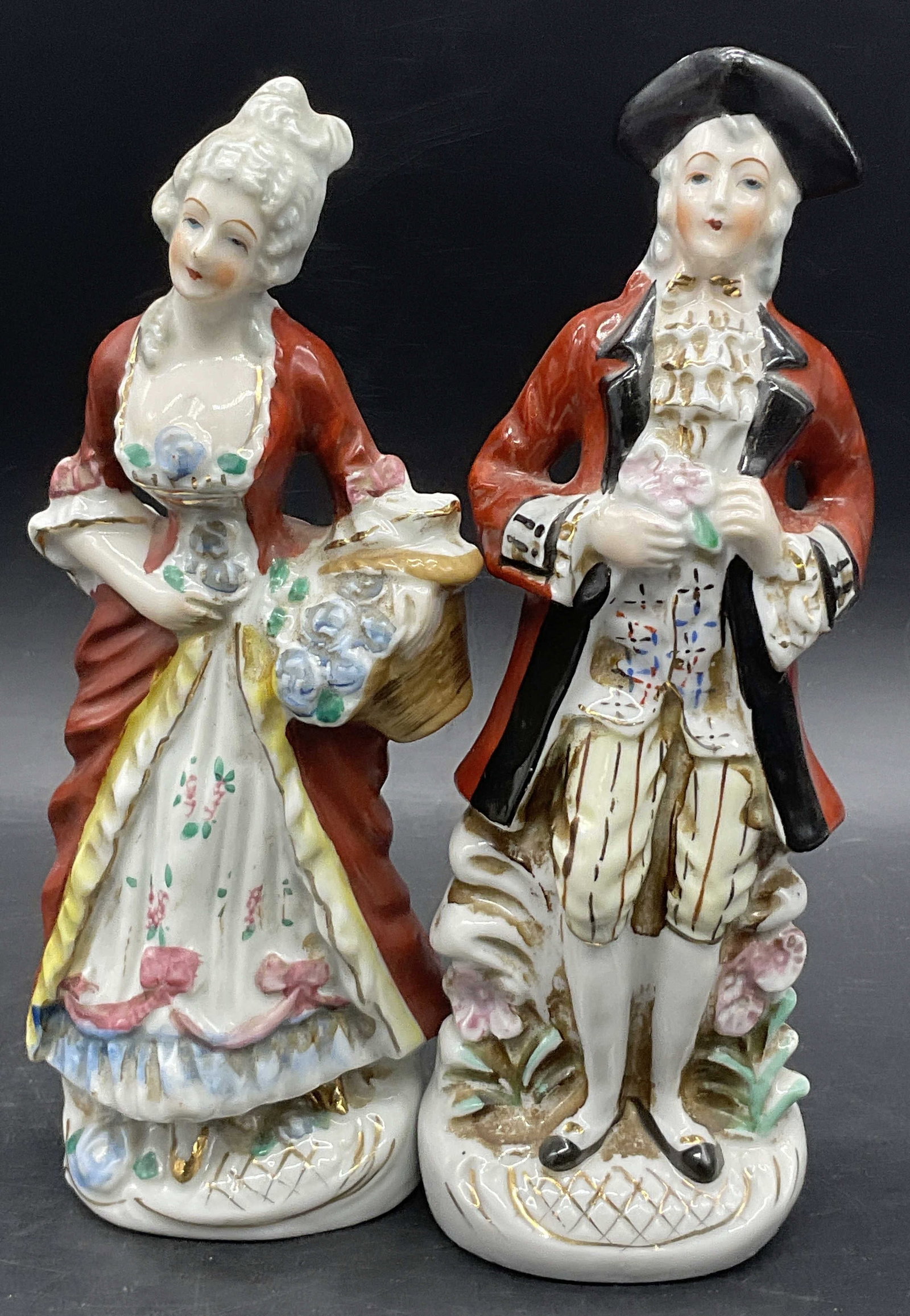 Set 2 Colonial Style Porcelain Man & Woman Figural: A Colonial / Victorian Style Porcelain Man Figural and A Colonial / Victorian Style Porcelain Woman Figural. Both figures wear multicolored clothing. Undersides marked MADE IN JAPAN. Taller figural me