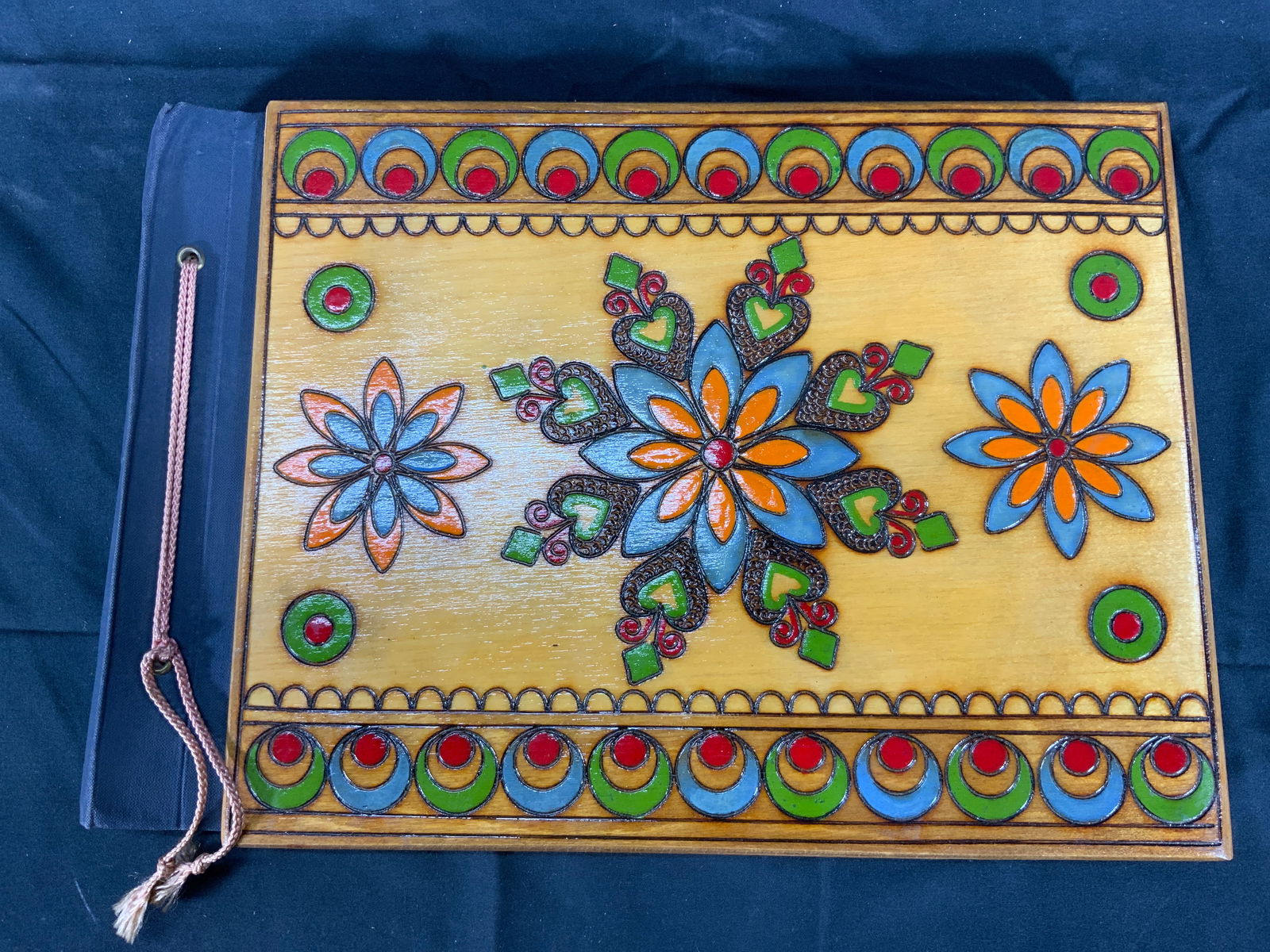 Traditional Polish Art in Arts & Crafts Album: Portfolio folder or photo album. Folder has wood covers with colored wood burning motifs of circles and flowers. Inside there are newspaper clippings along with traditional paper cutting collage and w