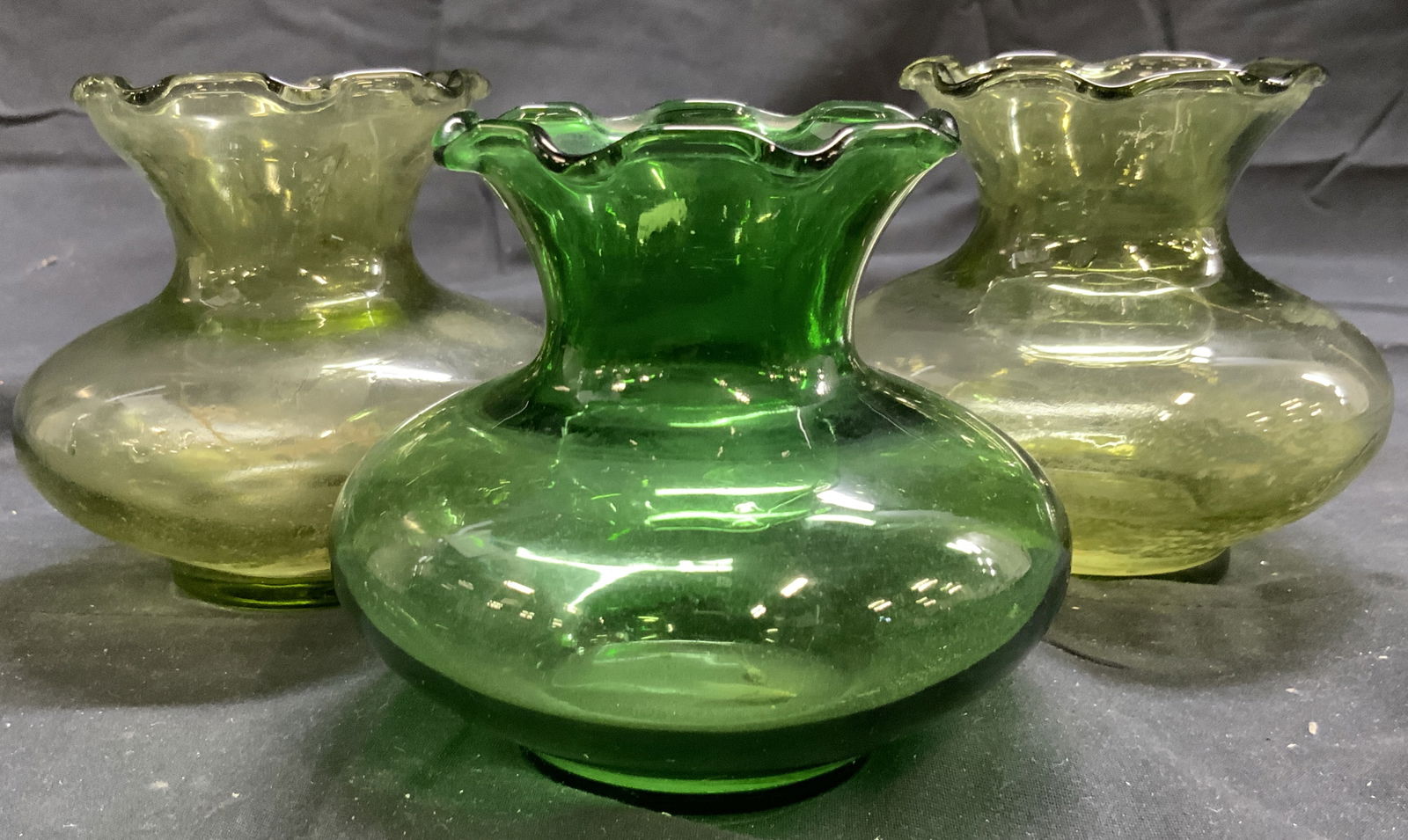 Lot 3 Art Glass Vases Green: Lot includes 3 vases. Each are green toned and glass. Vases each have handkerchief style rims. Vases each measure approximately 3.5 inches tall 3.75 inches wide. Art glass, vases, vessels, decorative