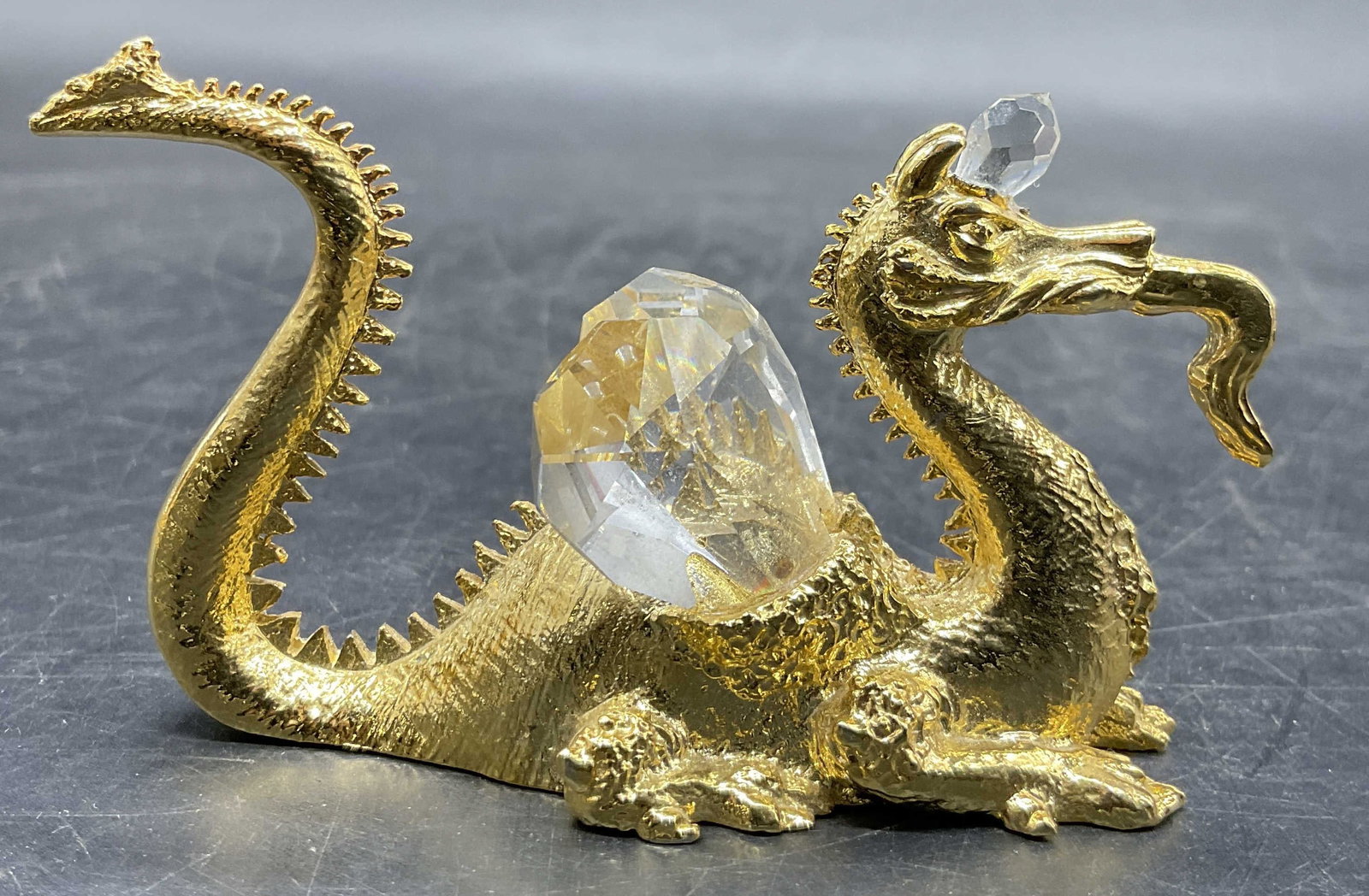 1984 SPOONTIQUES Vintage Gold Tn Crystal Dragon: A vintage gold tone metal dragon jeweled with faceted colorless crystals. Underside signed 1984 SPOONTIQUES. Measures approx. 1.75H x 3W in. Surface wear consistent with age, use, and exposure. Chippi