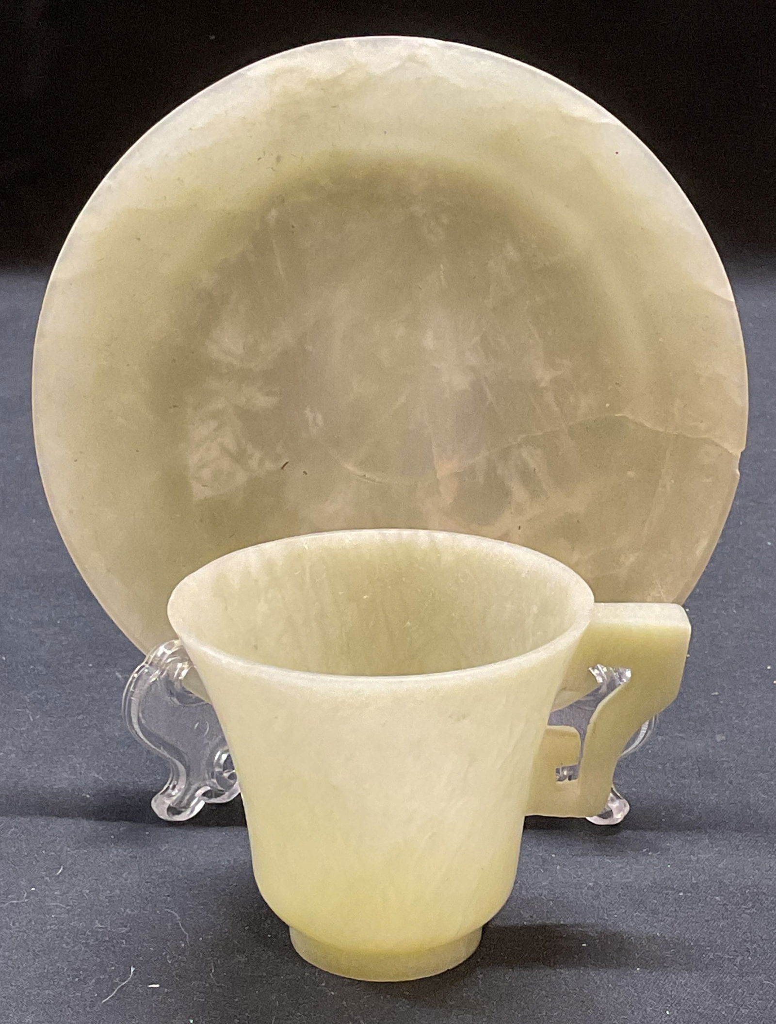 Carved Jadeite Demitasse Cup & Saucer: Carved jadeite or jade demitasses cup and saucer. Saucer measures approx 4.5 inches wide. Cup measures approx 2.5 x 2.25 inches. Wear including chip and crack to saucer. Demitasse cup and saucer, jade