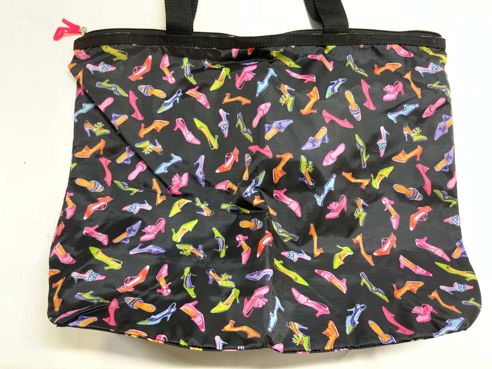Heel Pattern Zippered Nylon Tote W Interior Pockets: Tote is nylon. Piece is black with multi toned heeled shoe detail. Tote has black toned strap handles. Interior has 2 open pockets and 1 zippered pocket. Tote bag measures approximately 23 inches tall