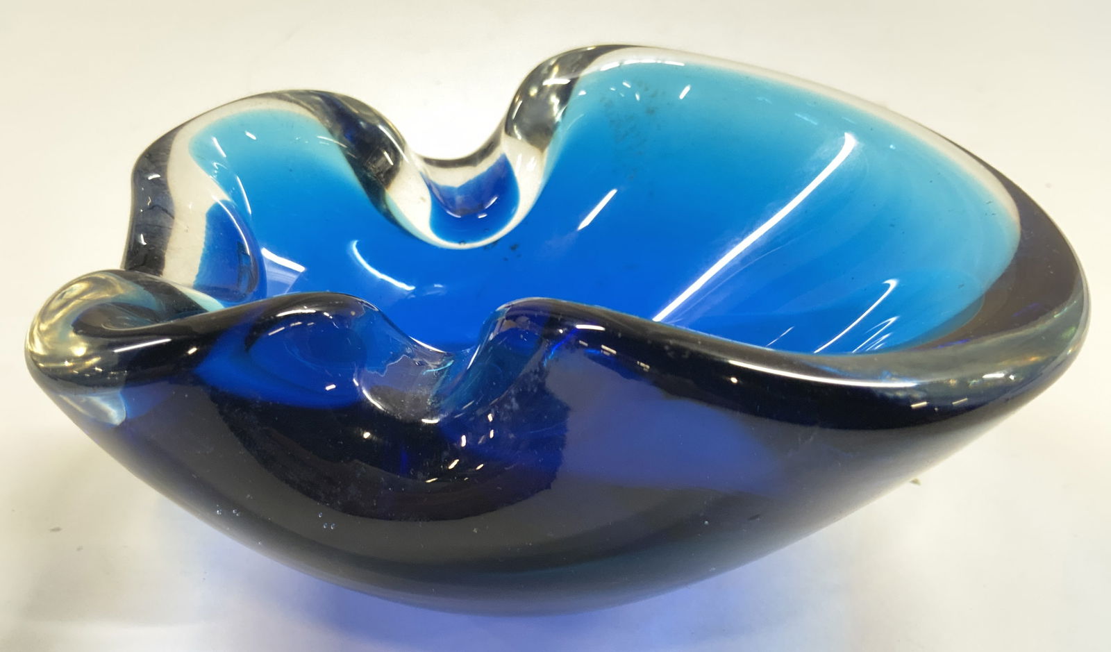 Thick Walled Art Glass Trinket Dish Blue: Trinket dish has thick walls. Piece is blue toned with clear areas. Dish is possibly hand blown. Areas of structure fold inward. Piece measures approximately 5 inches deep 4.75 inches wide 2.5 inches