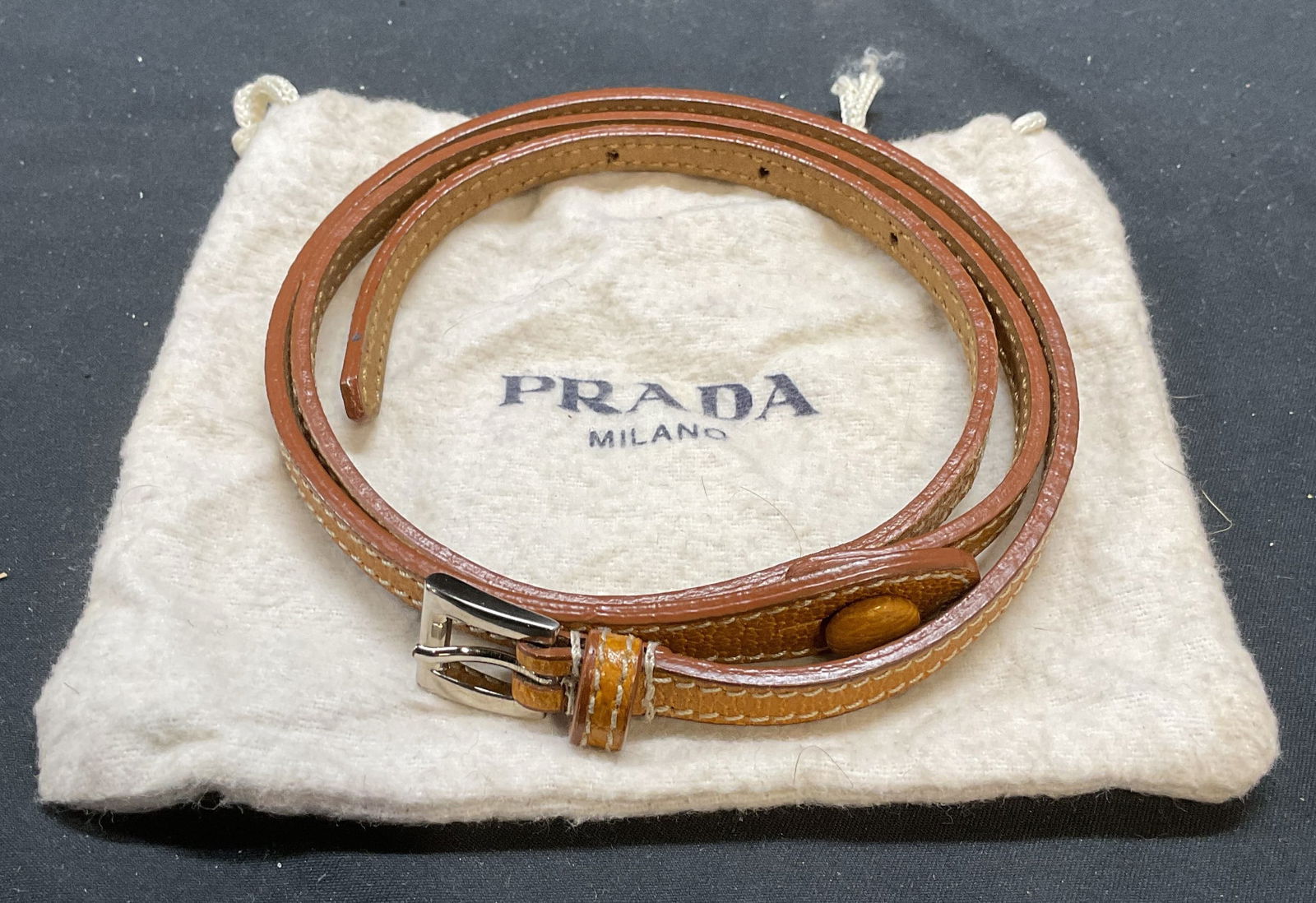 Prada Tan Leather Skinny Belt, Italy: Prada tan leather skinny belt. Two piece with button and silver tone buckle. Signed on leather and buckle. Made in Italy. Size 30. Includes dust bag. Some wear to leather including creasing observed.