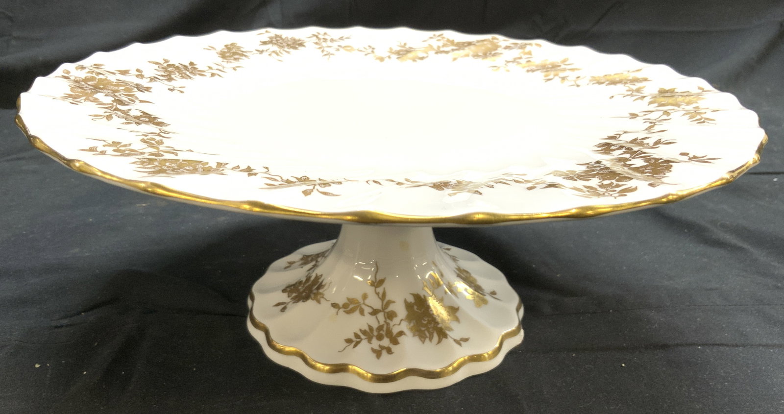 STAFFORDSHIRE ARISTOCRAT Fluted Porc Cake Stand: Underside is marked STAFFORDSHIRE ARISTOCRAT ENGLAND. Cake stand is white toned and porcelain with gilt floral, & leaf detail & rim. Cake stand is pedestaled. Piece is fluted. Cake stand measures appr