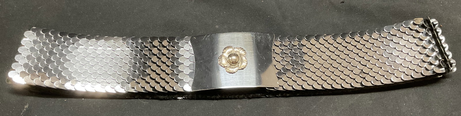 Silver Tone Metal Flower Buckle Stretch Belt: Stretch belt with woven fabric lining and fish scale style silver tone metal outer. Flower motif buckle. Measures approx 25 inches long. Material has some stretch. Surface wear including scratching. B