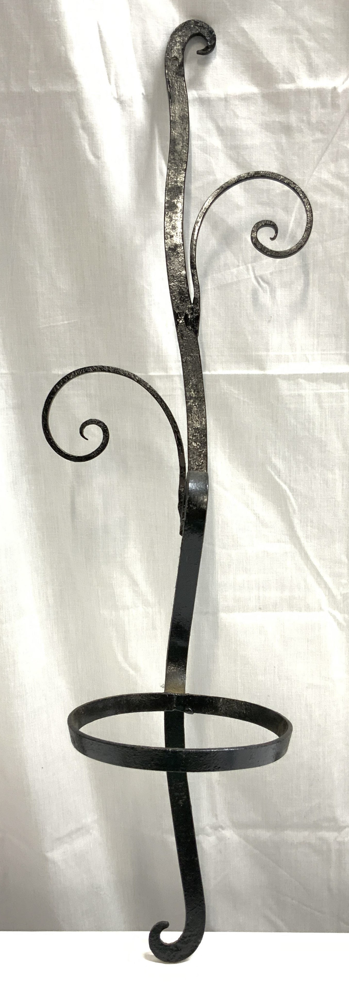Vintage Wall Mount Iron Plant Stands: Plant stand is vintage. Piece is black toned, appears to be iron. Plant stand has curl structures. Lower area of piece has ring for planter. Piece measures approximately 29.25 inches tall 8.75 inches 