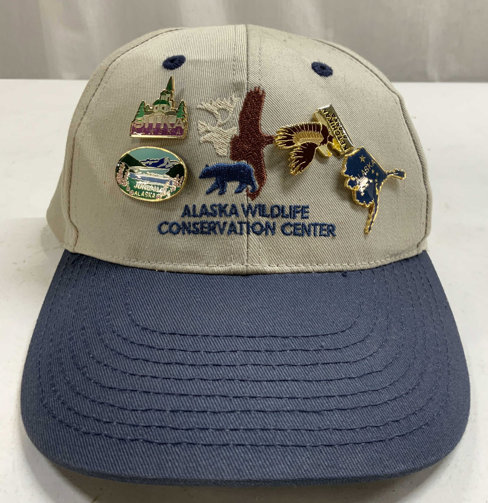 ALAKSA WILDLIFE CONSERV CENTER Cap W Pins: Cap reads ALASKA WILDLIFE CONSERVATION CENTER. Cap is cotton. Cap includes 4 pins (JUNEAU ALASKA pin, Alaska State Shape pin, Sitka Alaska Pin). Cap is adjustable. Piece measures approximately 6.25 in