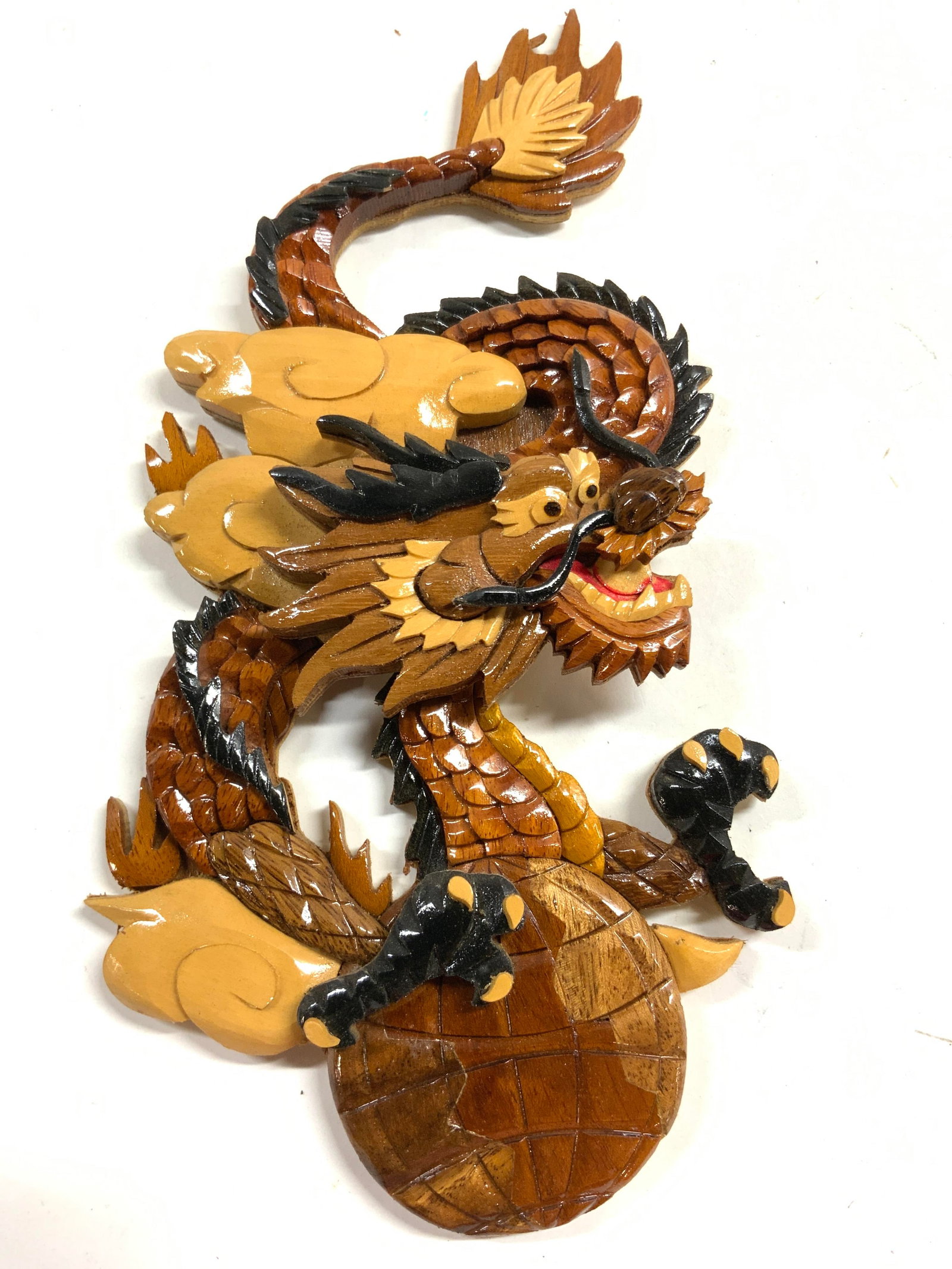 Carved Layered Wood Dragon Wall Decor: Piece is crafted from layered wood. Dragon figure has brown, tan, and black toned detail. Piece has intricate relief detail to show facial features, scales and claws. Piece measures approximately 11 i