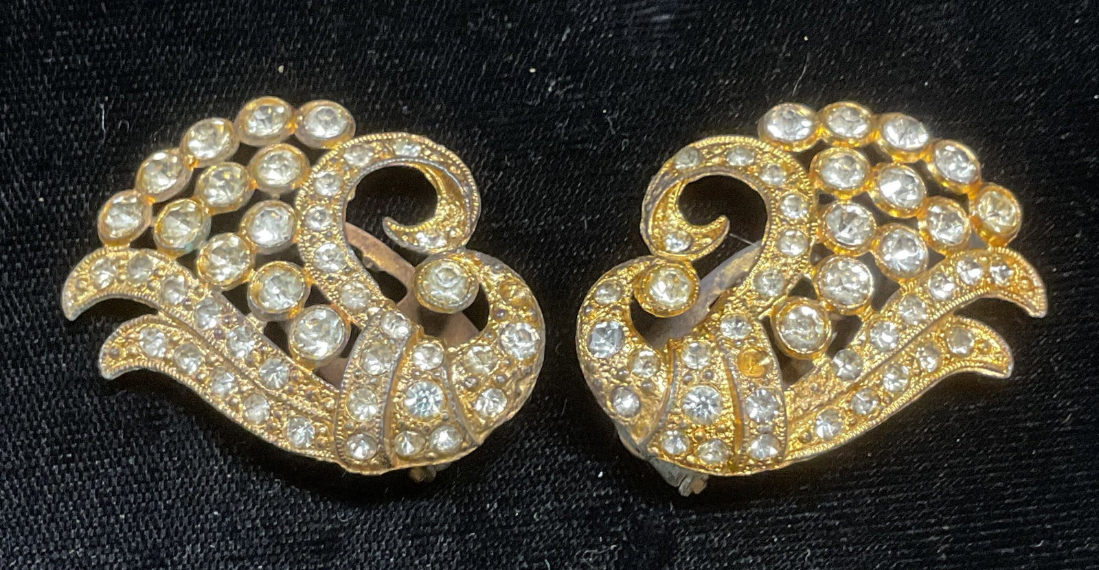 Pair Vintage Gold Tone Crystal Scroll Fur Clips: Pair of vintage gold tone scroll motif fur, sweater, and dress clips with colorless crystal. Measures approx 1.5 x 1.25 inches. Some wear including scratching observed. Some crystals need replacement.