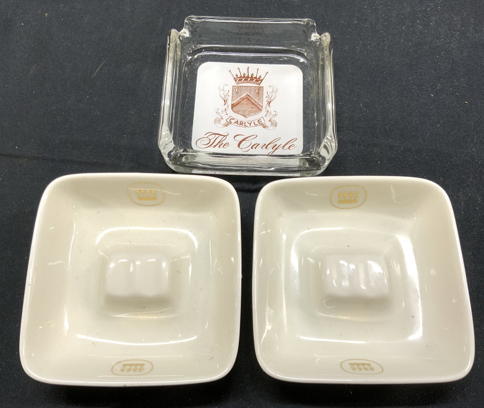 Lot 3 Porc & Gls Trinket Dishes: Lot includes 2 porcelain trinket dishes & 1 glass trinket dish trademarked THE CARLYLE. Porcelain dishes are cream with gilt detail. Each measures approximately 3.75 inches square, 1.25 inches tall. T