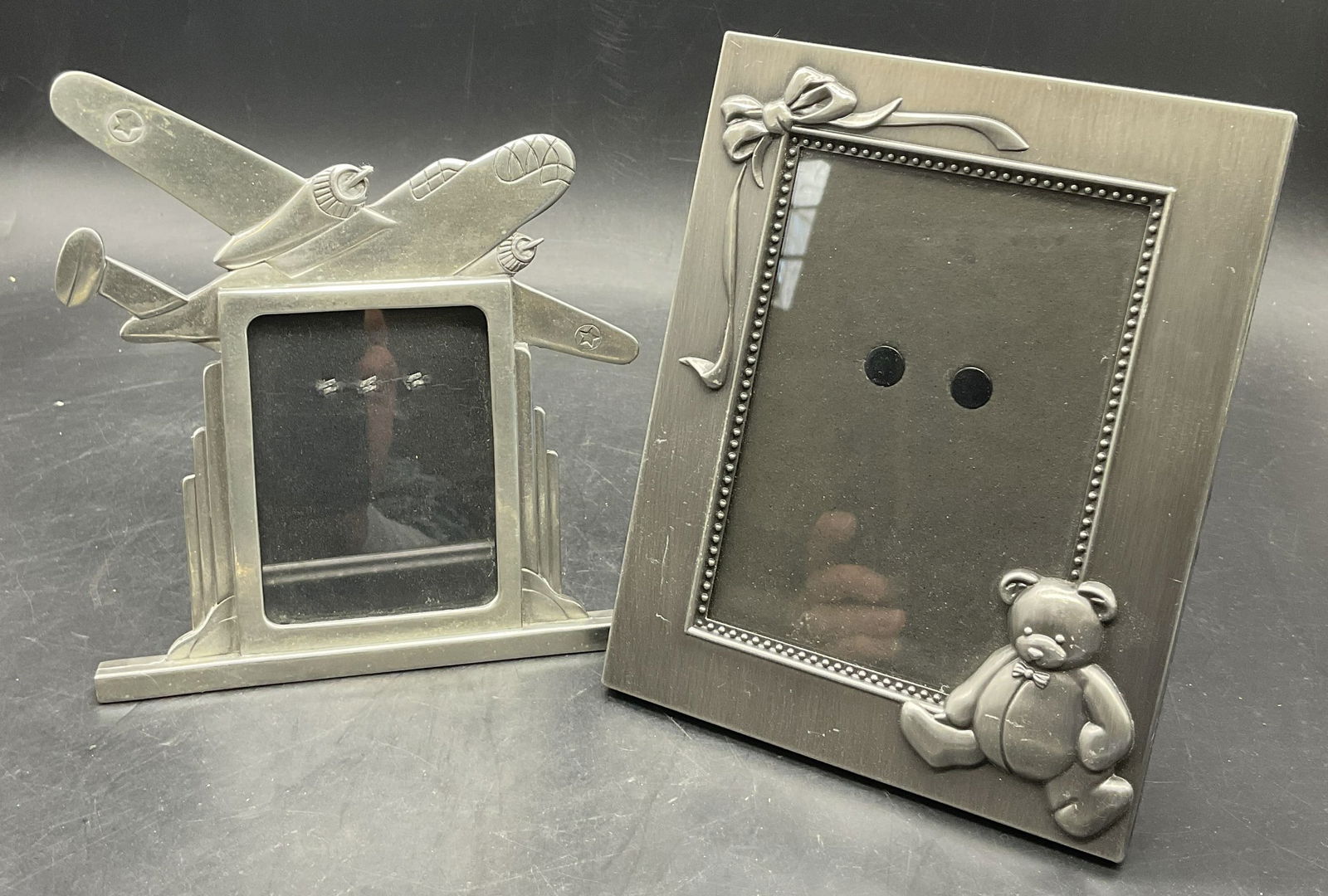 Lot 2 Airplane & Teddy Bear Motif Picture Frames: Two silver tone metal picture frames with kickback stands. Teddy bear and airplane motif to the pieces. Larger frame measures approx. 7L x 5.5W in. Surface wear and discoloration present. home decor,