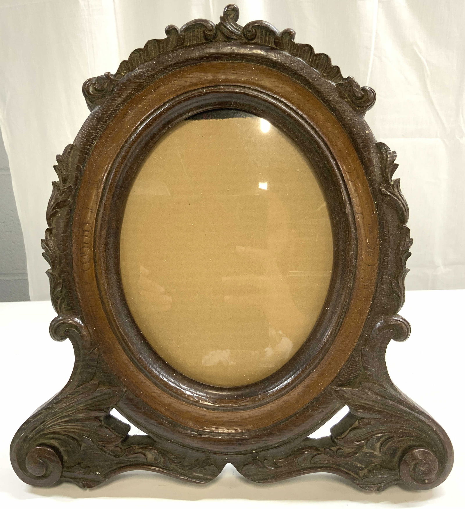 Vntg Ornate Carved Wood Standing Picture Frame: Picture frame is vintage and wooden. Frame is brown toned. Piece has carved scroll & acanthus leaf detail. Frame window has oval form. Frame has stand on backside. Piece measures approximately 16 inch