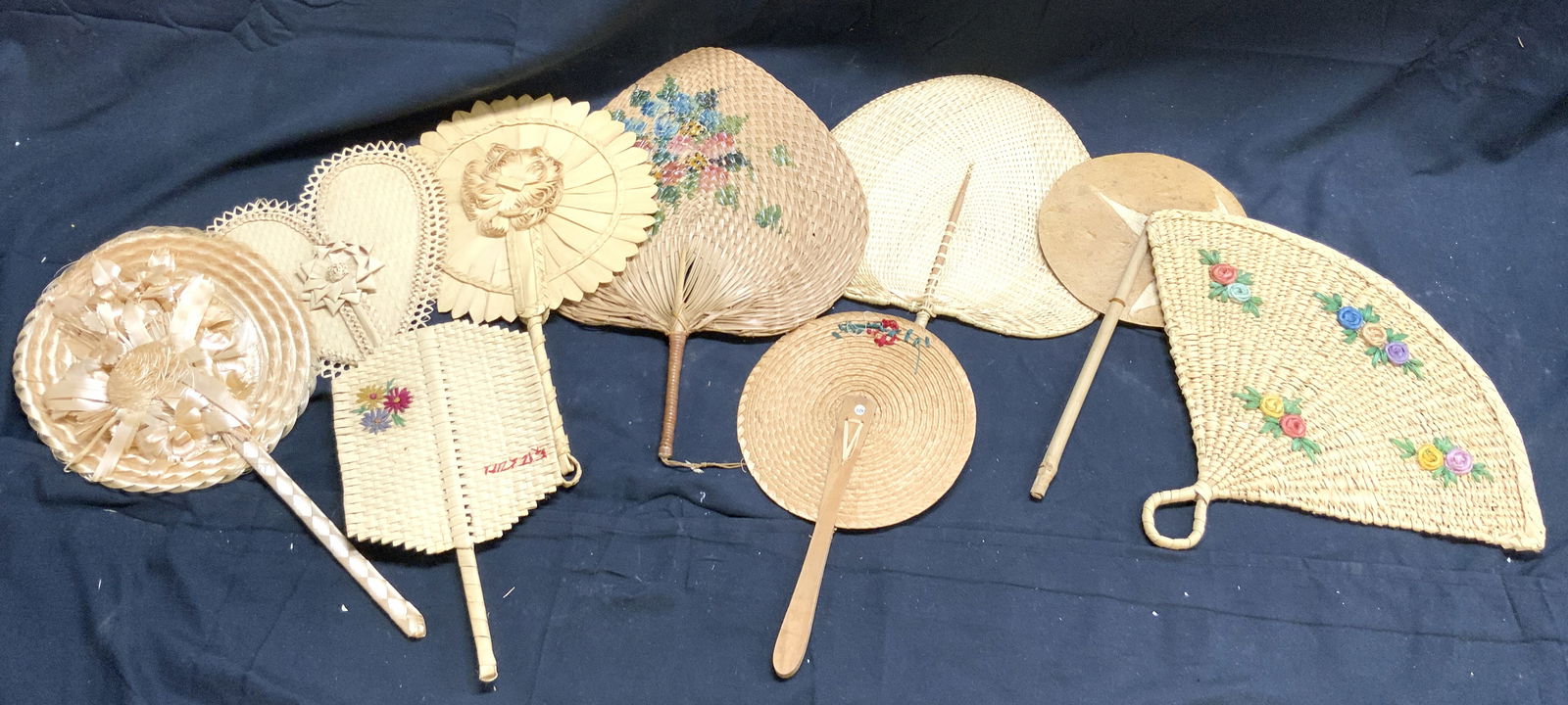 Lot 9 Assorted Woven Wicker Hand Fans: Lot includes 9 fans. Each have varying tan tones. Some pieces have floral and leaf detail. Hand fans appear to possibly be vintage. Largest piece measures approximately 15 inches tall 10 inches wide.
