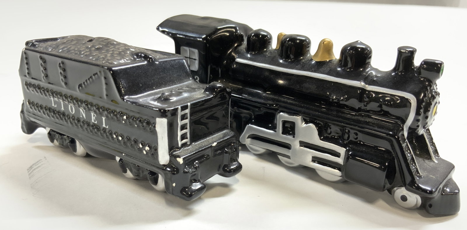 LIONEL Train Car Porc Salt & Pepper Shakers: Underside reads LIONEL LLC ENESCO CORPORATION. Lot includes 2 shakers. Each are black toned and porcelain. Sides of one shaker reads LIONEL. Steam engine form shaker reads 773 on sides. Steam engine s
