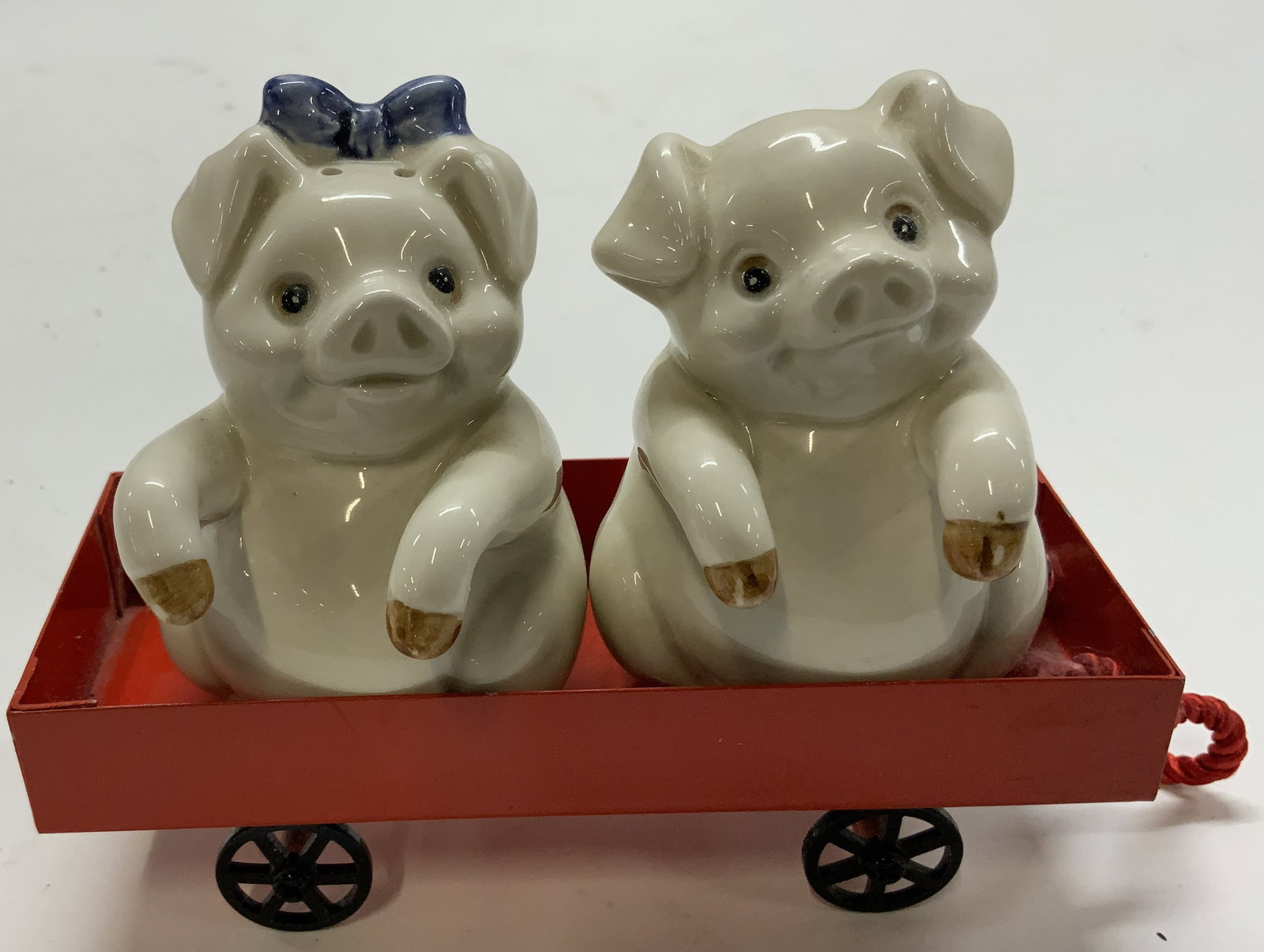 Vtg Porc S/P Shakers Pigs in Wagon 3pcs: This Porcelain set of pig salt and pepper shakers features a red wagon for them to sit in. They are approximately 3 1/4 in height and are hand painted white , with one having a blue bow on its head. K