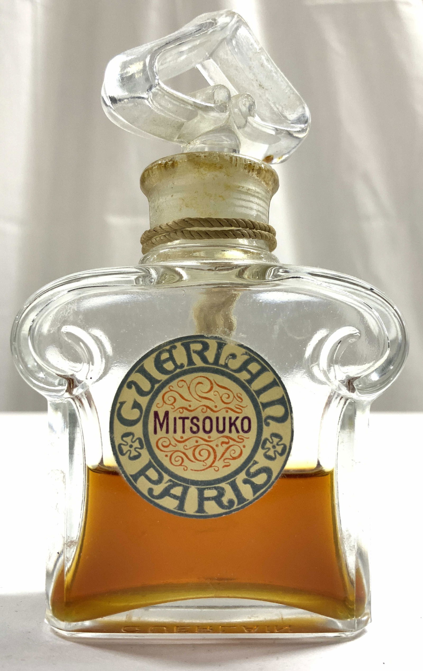 GUERLAIN Mitsouko Eau De Toilette: Label reads GUERLAIN MITSOUKO PARIS. Mitsouko Eau de Toilette by Guerlain is a Chypre Fruity fragrance for women. Bottle is partially full. Mitsouko Eau de Toilette was launched in 1919. The nose behi