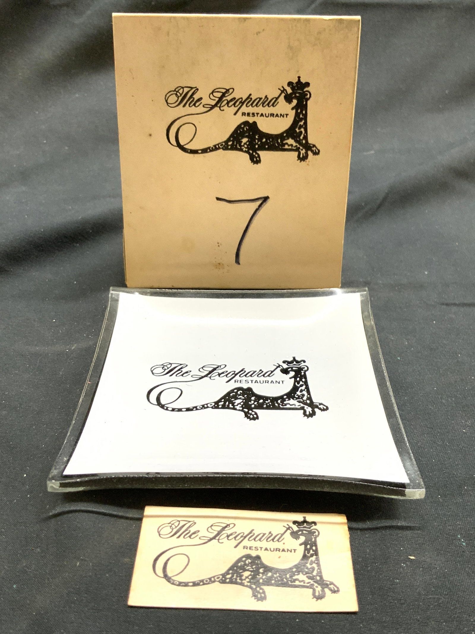 THE LEOPARD RESTAURANT Trink Dish Tbl Card & More: Lot includes 1 table card matchbox, numbered 7, 1 trinket dish & 1 card. Each piece reads THE LEOPARD RESTAURANT. Trinket dish is glass. Table card has matchbox inside base. Table card matchbox measur