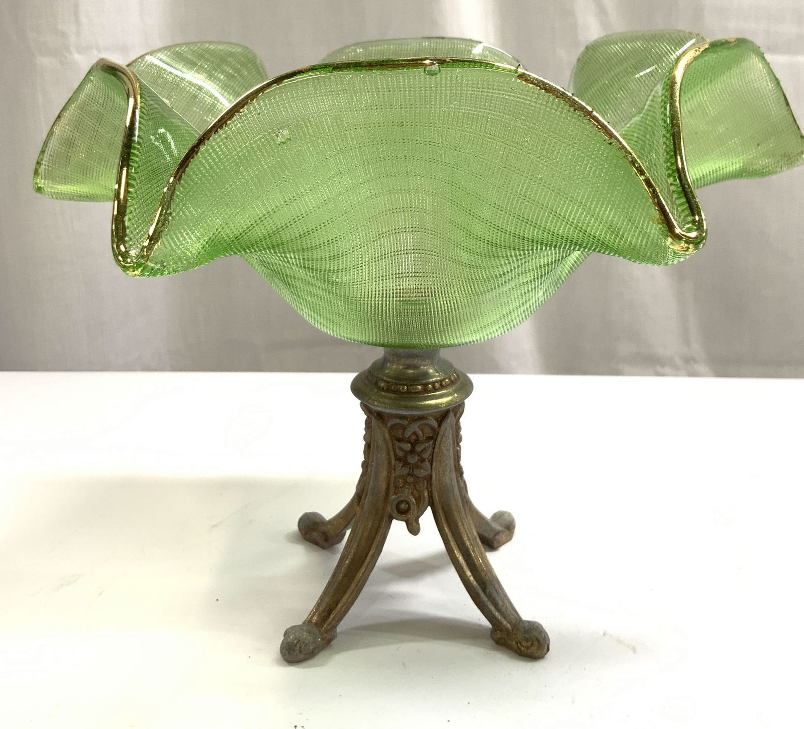 Vntg Gilt Metal Base Handkerchief Glass Vessel: Vessel is vintage. Piece is green toned handkerchief glass with gilt rim. Vessel has gilt metal base with 4 feet, floral and leaf detail. Glass area has geometric relief pattern detail. Piece measures
