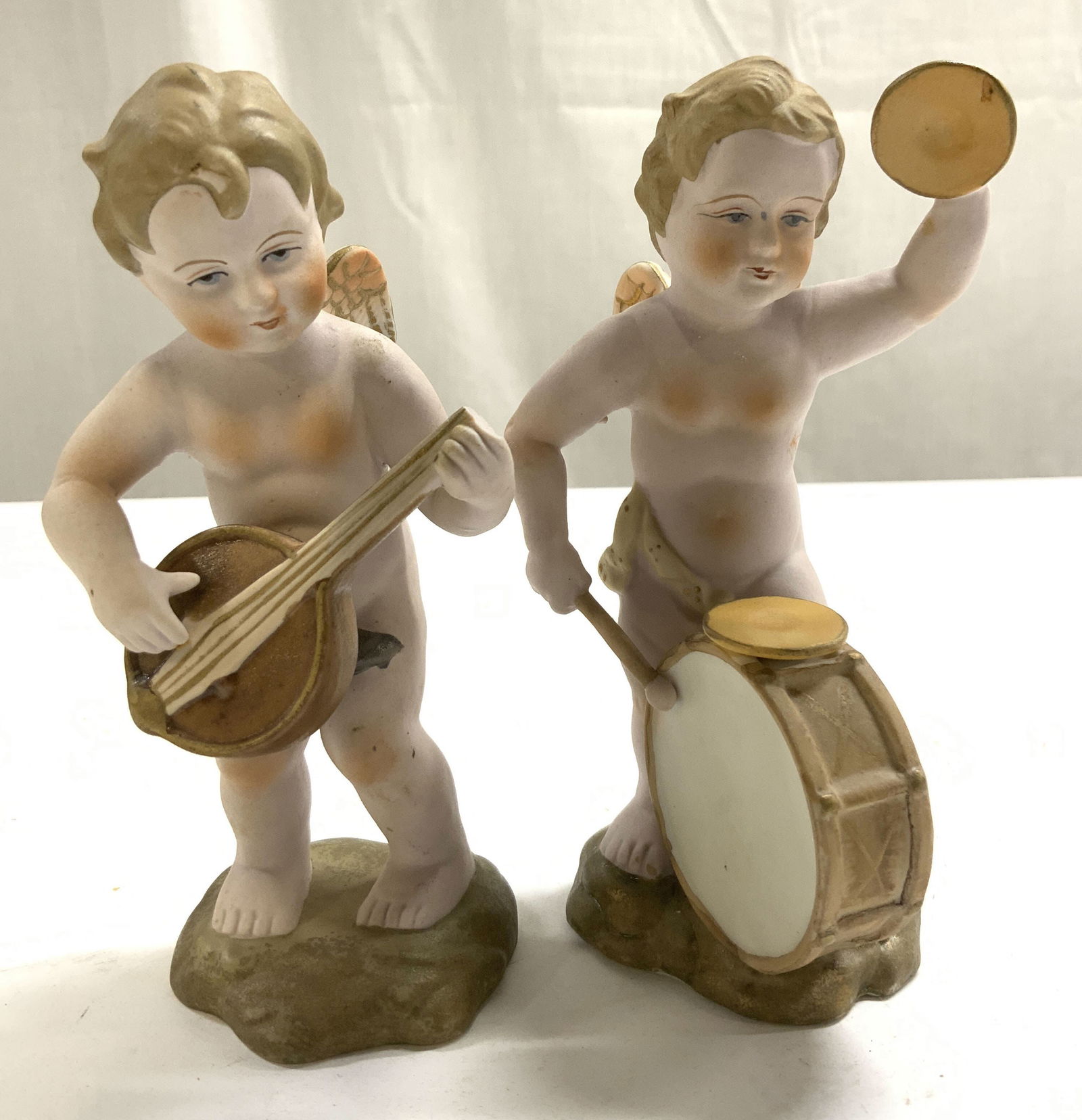 ARDALT Lot 2 Hand Painted Bisque Cherub Figures: Tags on Undersides reads ARDALT HAND PAINTED. Lot includes 2 cherub figures. One with drums, and 1 with ukulele. Each are hand painted. Slightly larger cherub figure measures approximately 5.5 inches