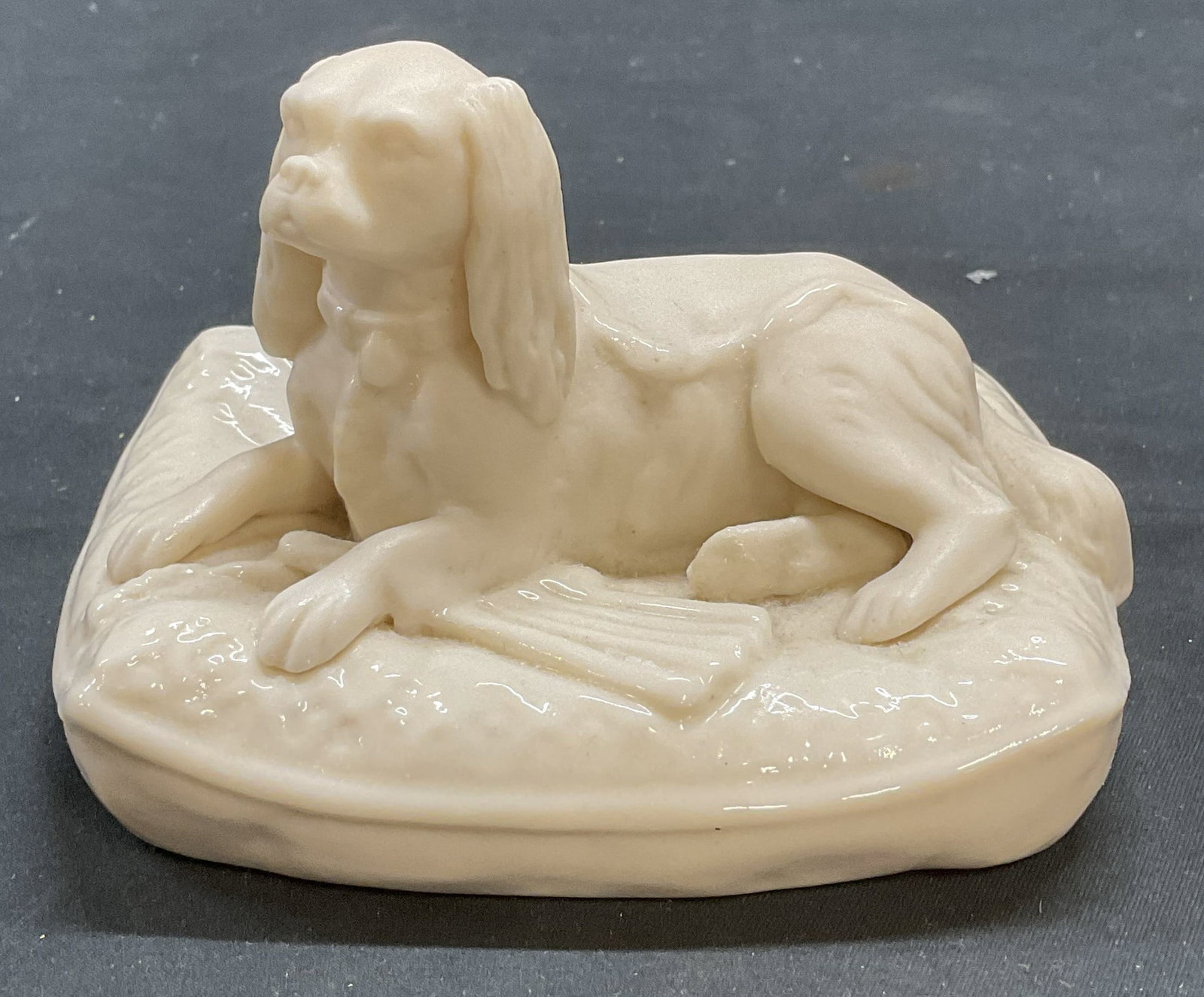 BELLEEK Porcelain Spaniel Dog Figural Ireland: BELLEEK porcelain spaniel dog on cushion figural. White matte and luster glaze. Signed on underside. Made in Ireland. Measures approx 4.5 x 3.75 x 3 inches. Some wear including scratching observed. BE