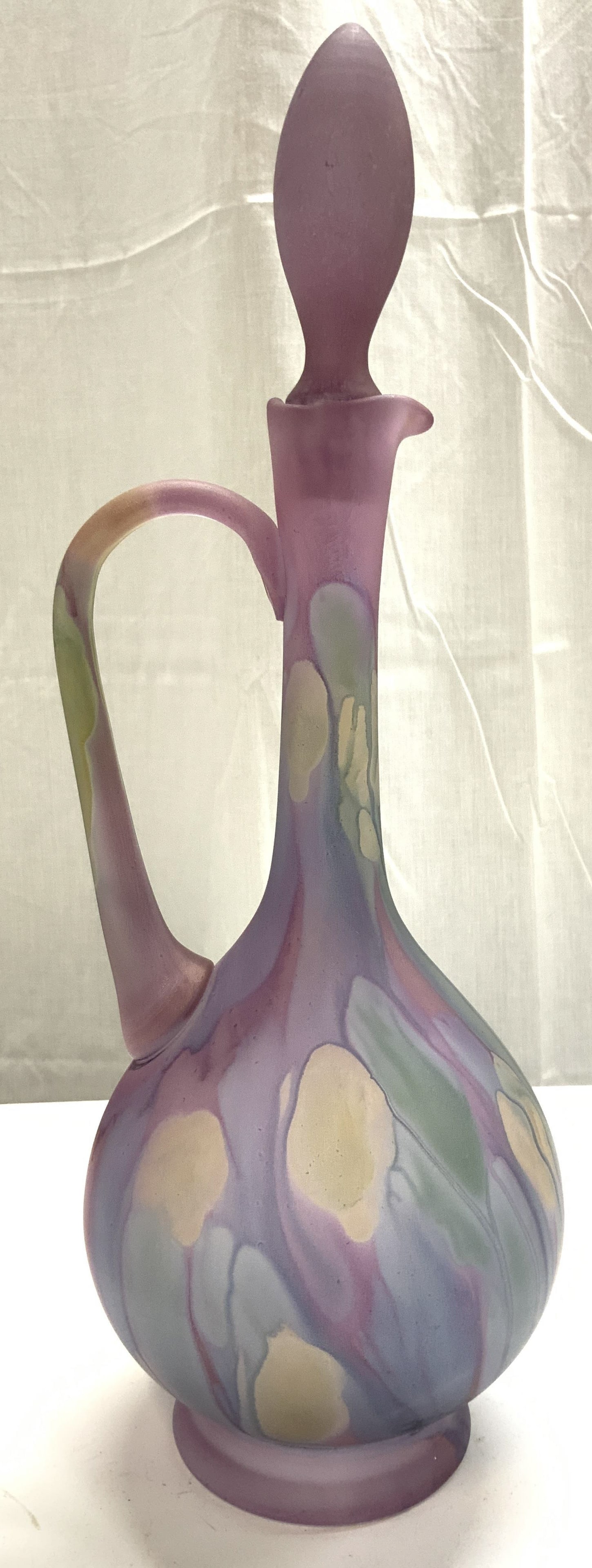 RUEVEN Nouveau Art Glass Ewer Decanter W Stopper: Decanter appears to be RUEVEN. Piece is glass. Ewer includes stopper. Piece has purple, yellow, & green toned paint drip detail. Piece is footed. Nouveau Art glass decanter. Piece measures approximate