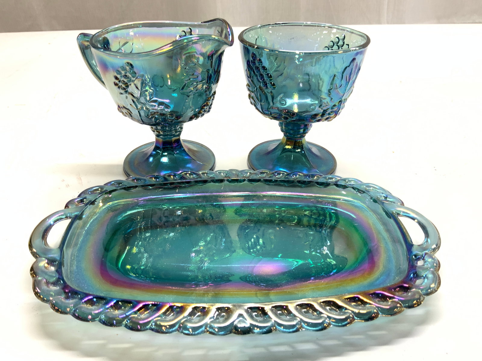 Set 3 Carnival Gls Creamer Sugar & Serving Dish: Pieces appear to be by INDIANA GLASS COMPANY (no apparent markings) Lot includes 1 serving dish 1 creamer dish & 1 sugar dish. Carnival glass tabletop. Creamer and sugar dishes are pedestaled and have