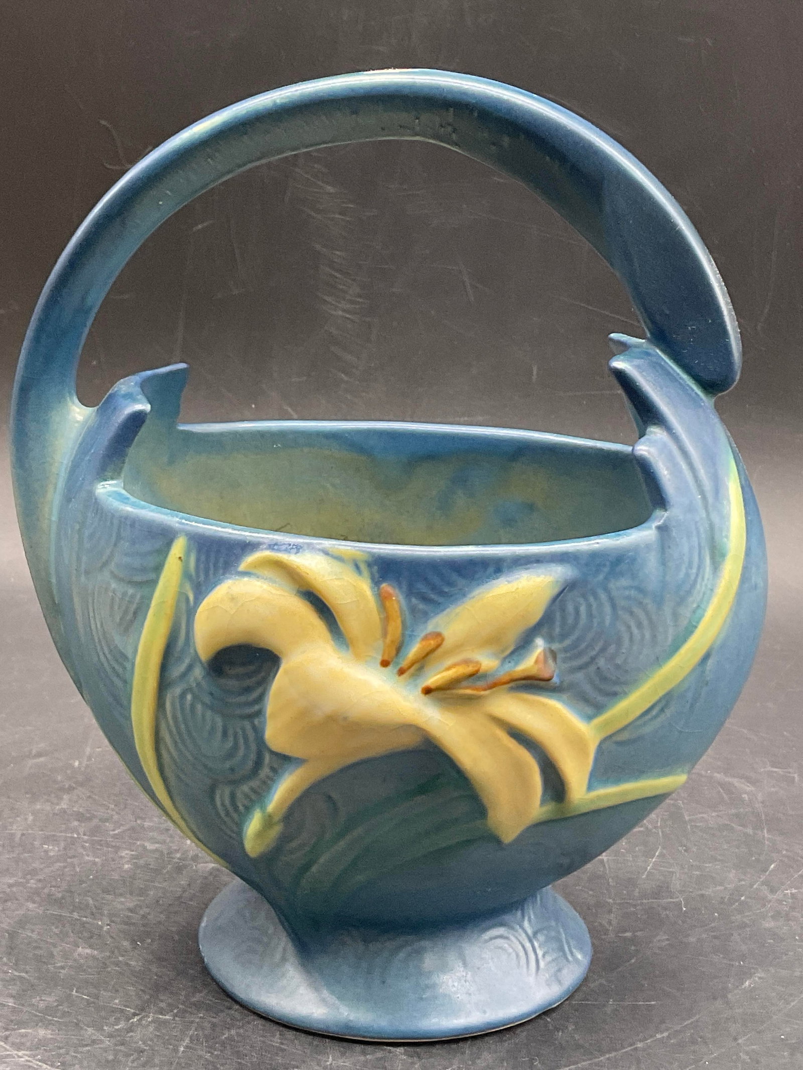 ROSEVILLE USA 3937 Zephyr Lily Pottery Basket: ROSEVILLE USA 3937 Zephyr Lily Pottery Basket. Raised lily to the obverse and reverse. Primarily blue, yellow, green, and brown hues. Underside signed ROSEVILLE USA 3937. Measures approx. 7.5H x 5.75W