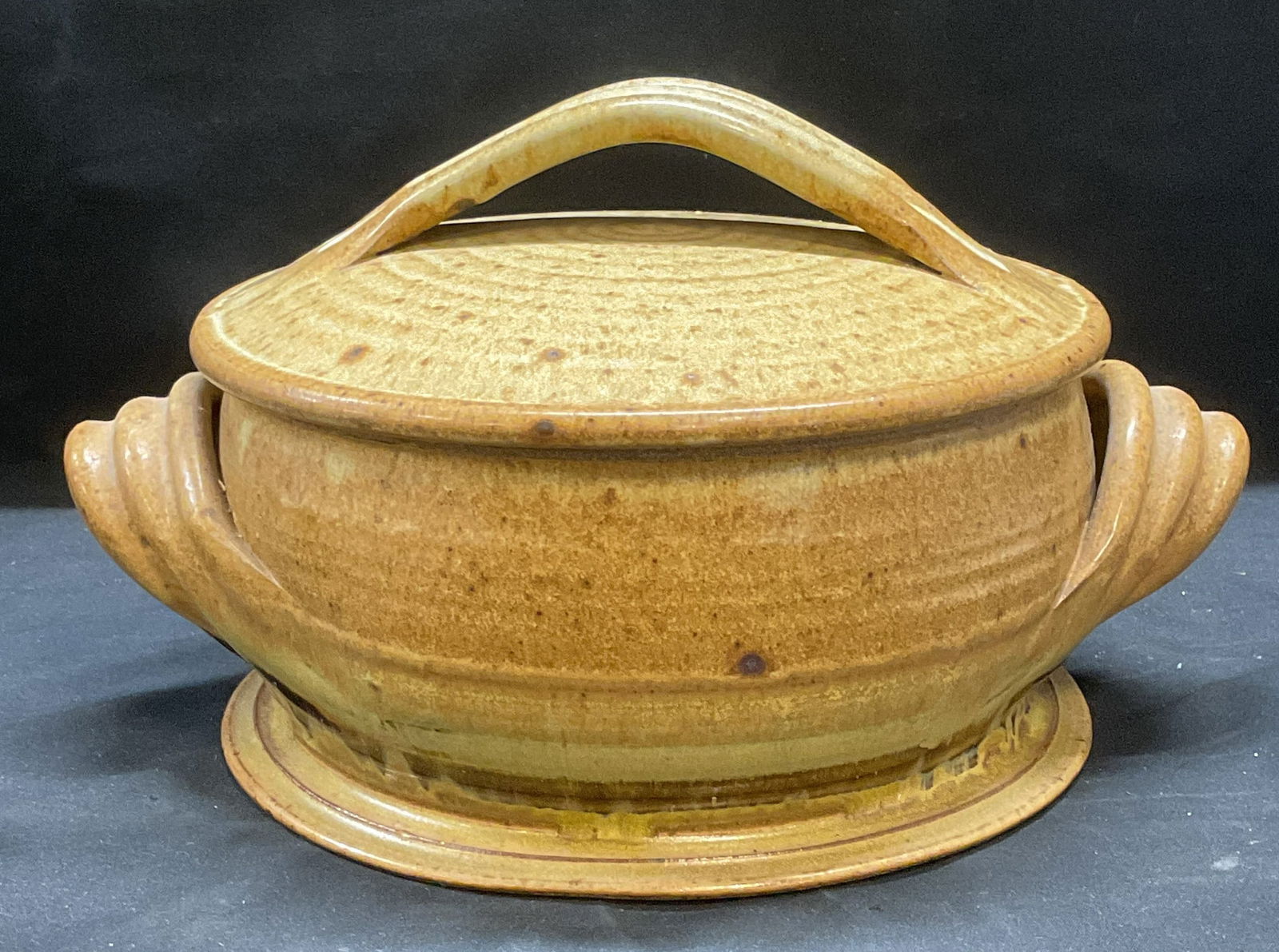 Chandler Handmade Beige Stoneware Covered Bowl: Stamped Chandler handmade stoneware bowl with lid. Flared footed base with double handles. Lid with handles. Speckled glaze in beige. Ribbed design throughout. Possibly antique. Stamped on underside,