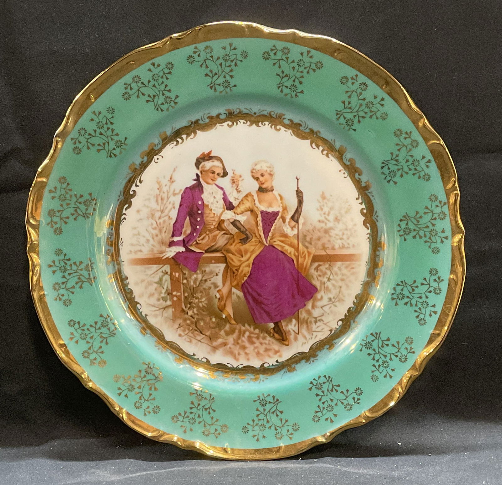KPM Green Gilt Porcelain Courting Couple Plate: KPM porcelain display plate. Courting couple motif. Green border with gilt floral and scroll decoration and scalloped rim. Signed on underside. Measure approx 10.25 inches wide. Some wear consistent w